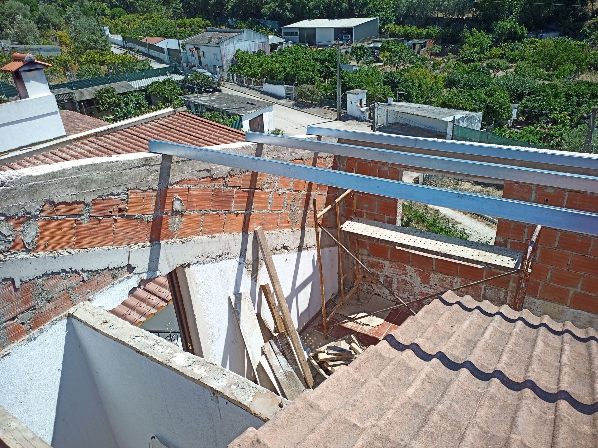 Terraço em construção com paredes de tijolos aparentes, vigas de metal e vista para a cidade.