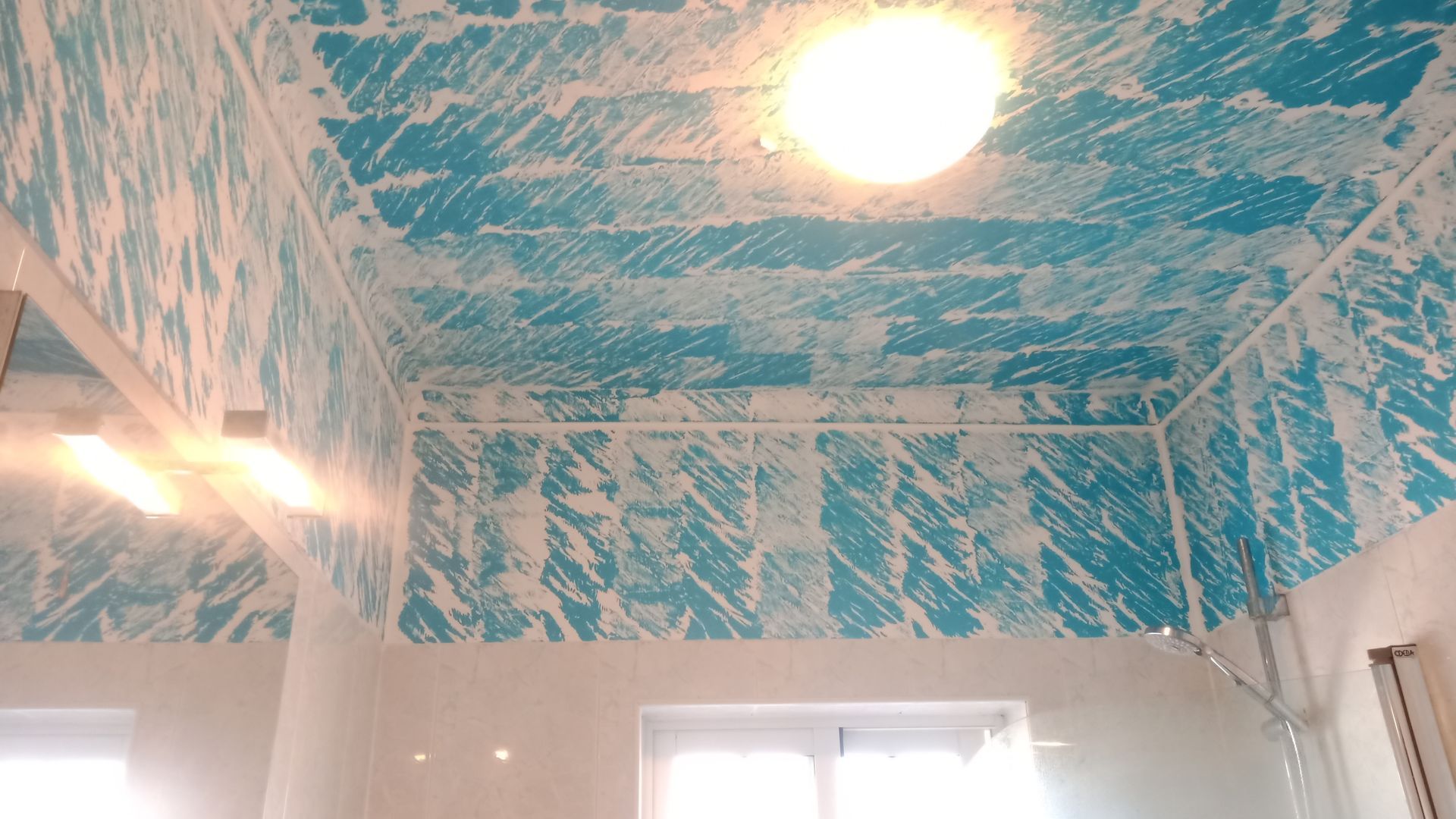 Quarto com teto e paredes estampadas em azul e branco, luminária e janelas.