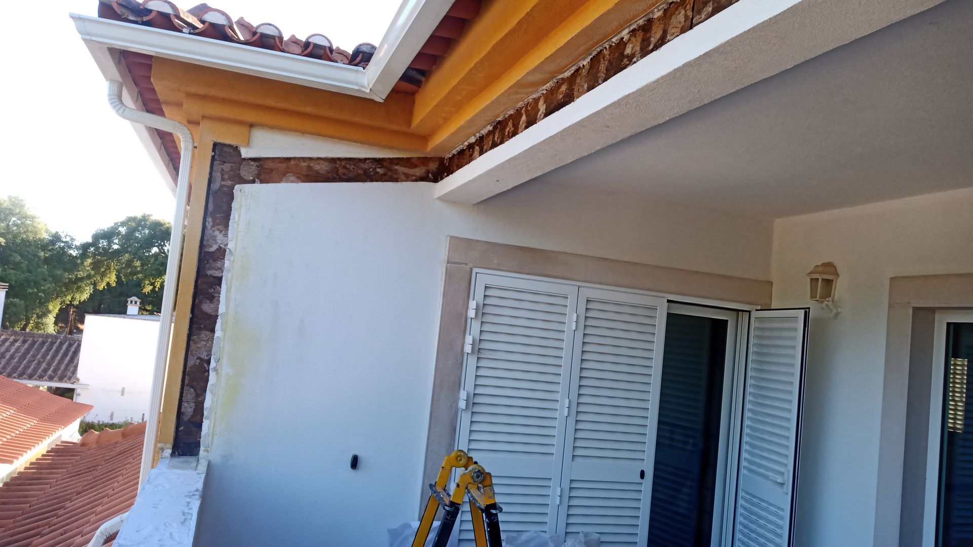 Fachada externa de prédio com varanda branca, venezianas e acabamento em madeira sob um telhado.