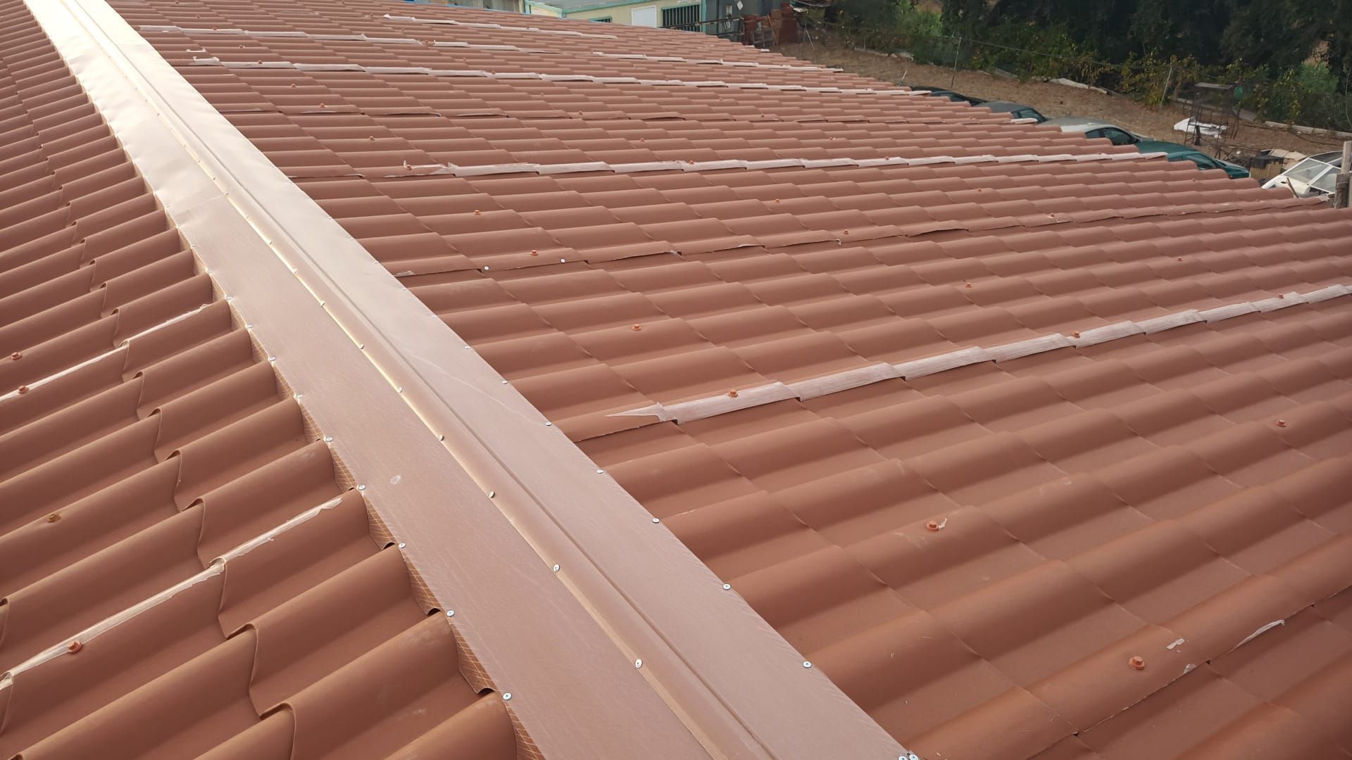 Telhado de metal ondulado marrom com uma faixa metálica no centro.