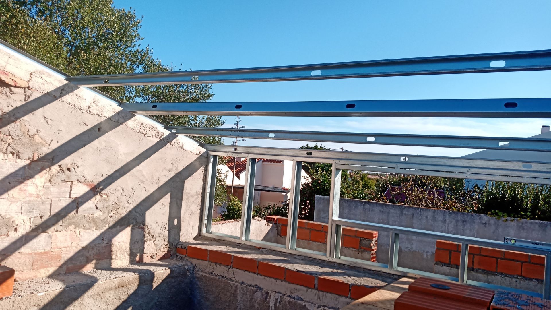 Estrutura metálica sobre parede de tijolos, sob um céu azul límpido.