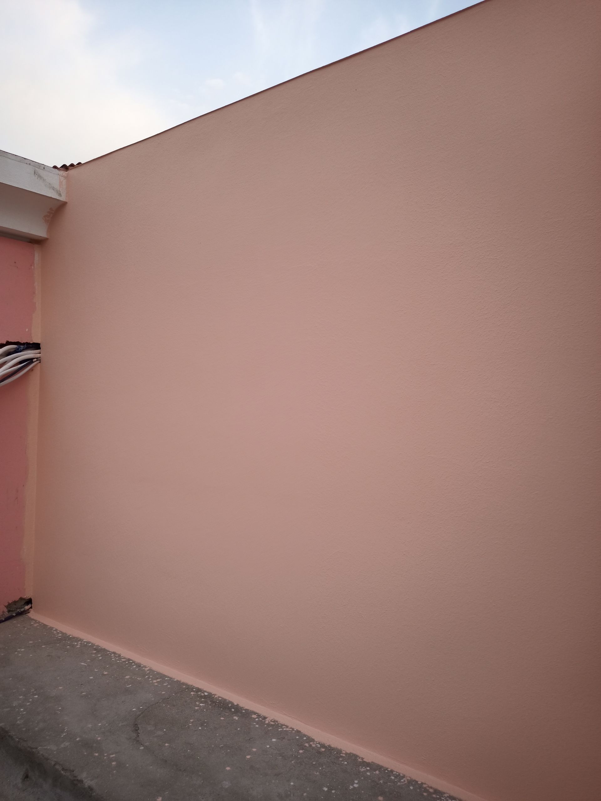 Parede externa cor de pêssego com superfície texturizada, possivelmente estuque, contra um céu nublado.