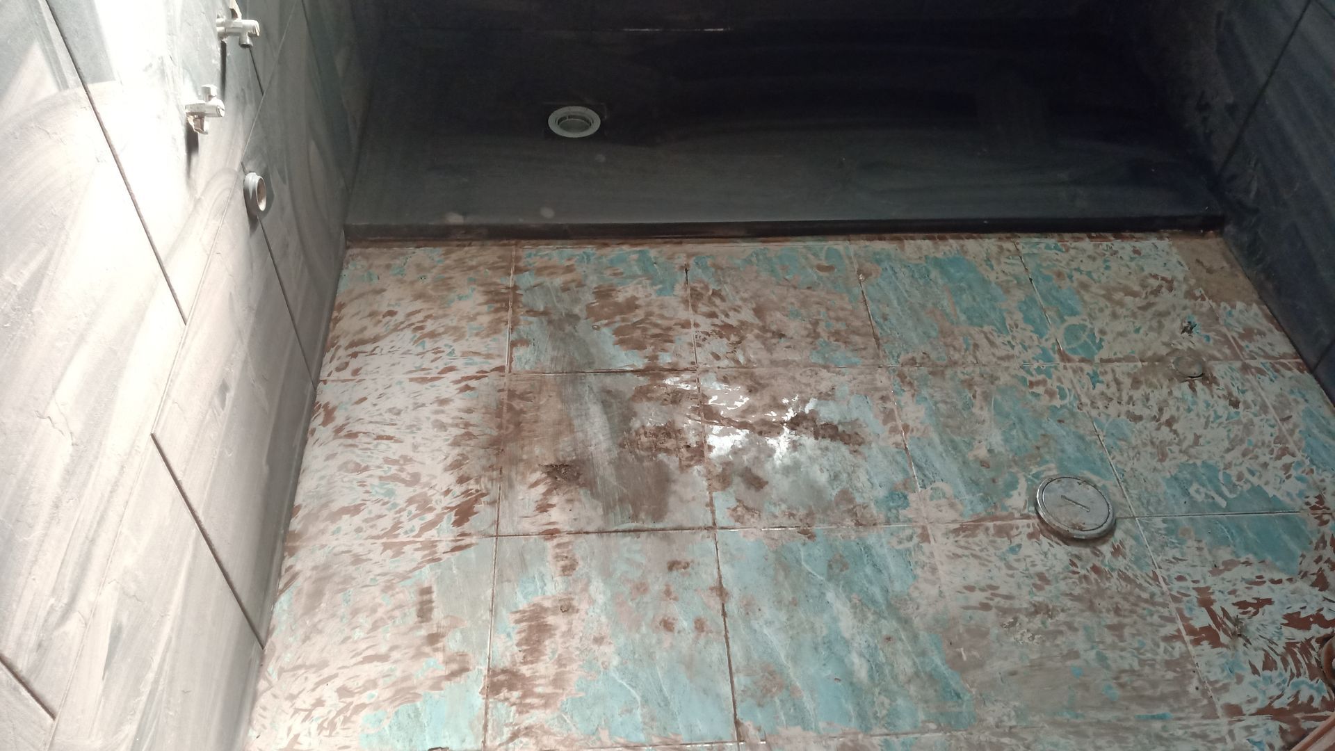 Interior do chuveiro escuro com paredes de azulejo e piso corroído. Chuveiros na parede.