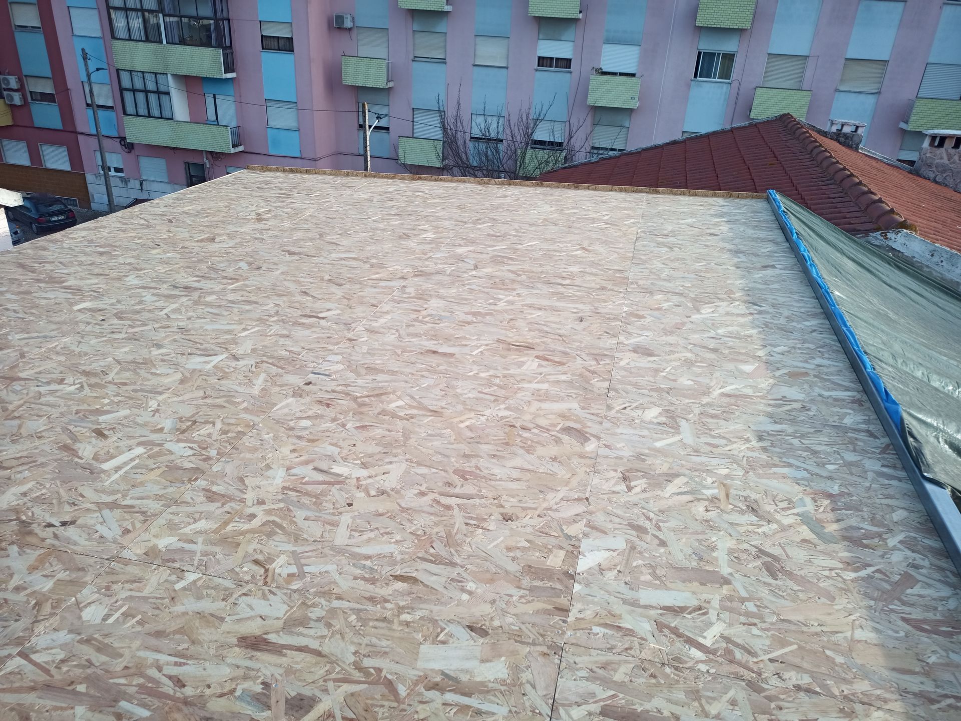 Telhado com painéis de madeira, construção em andamento, prédios ao fundo.