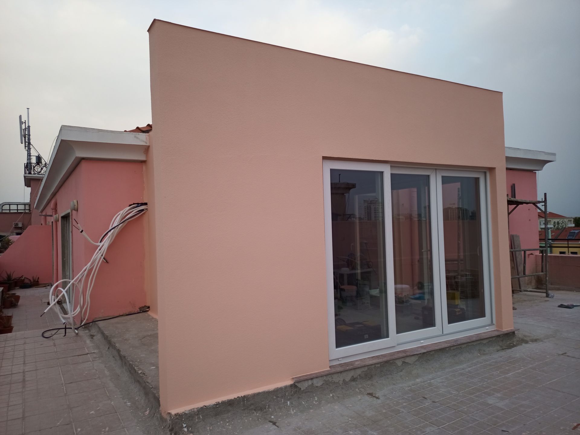 Prédio rosa com portas e janelas de vidro com moldura branca, antenas no telhado, céu nublado.
