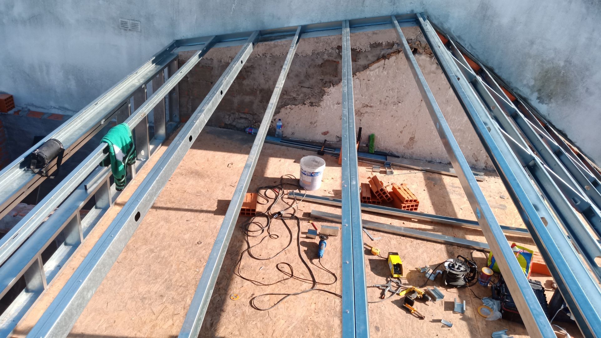 Estrutura metálica para teto ou cobertura. Ferramentas e materiais estão espalhados pela área de construção.