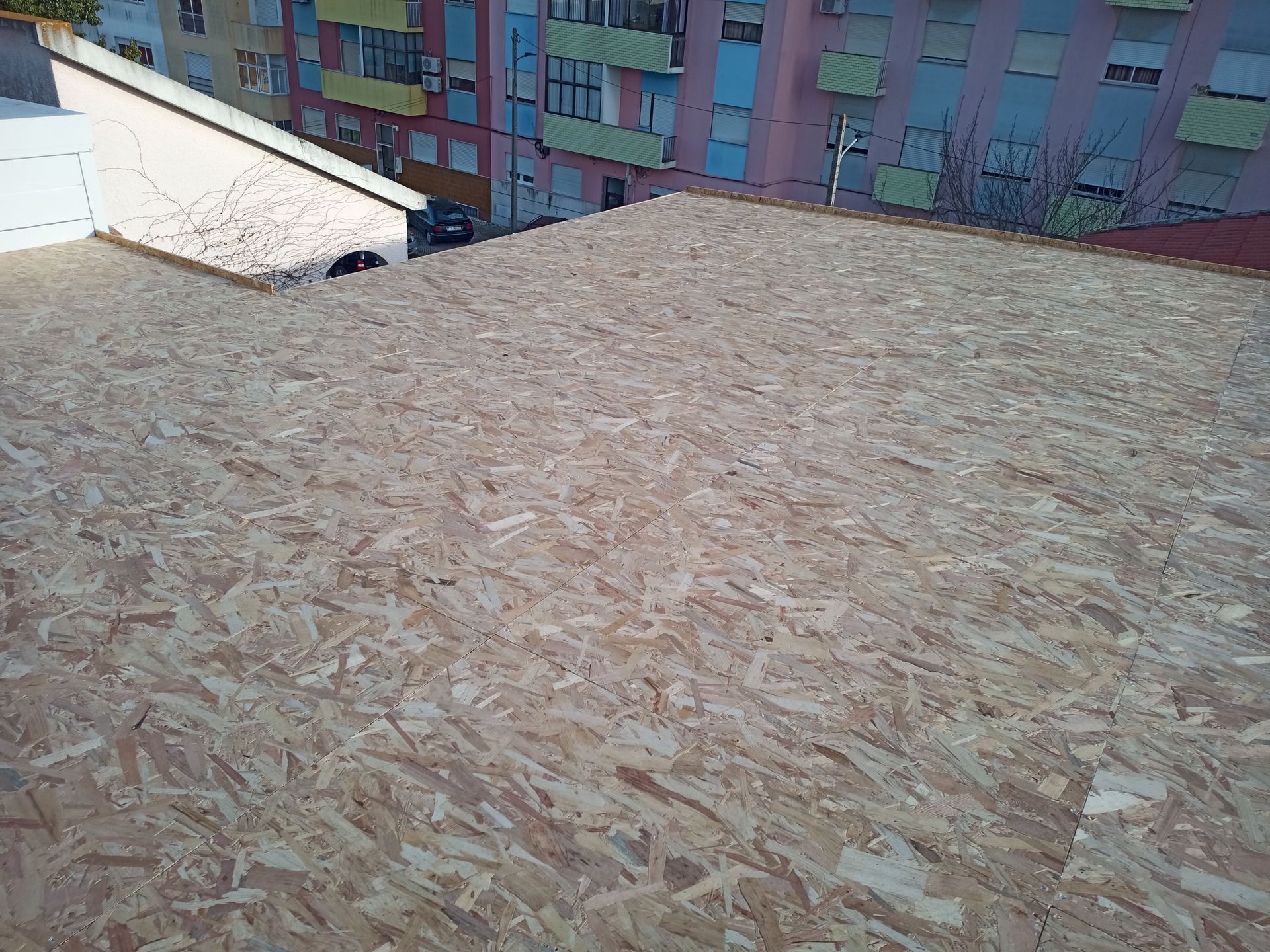 Revestimento de OSB no telhado de um edifício, com prédios de apartamentos ao fundo.