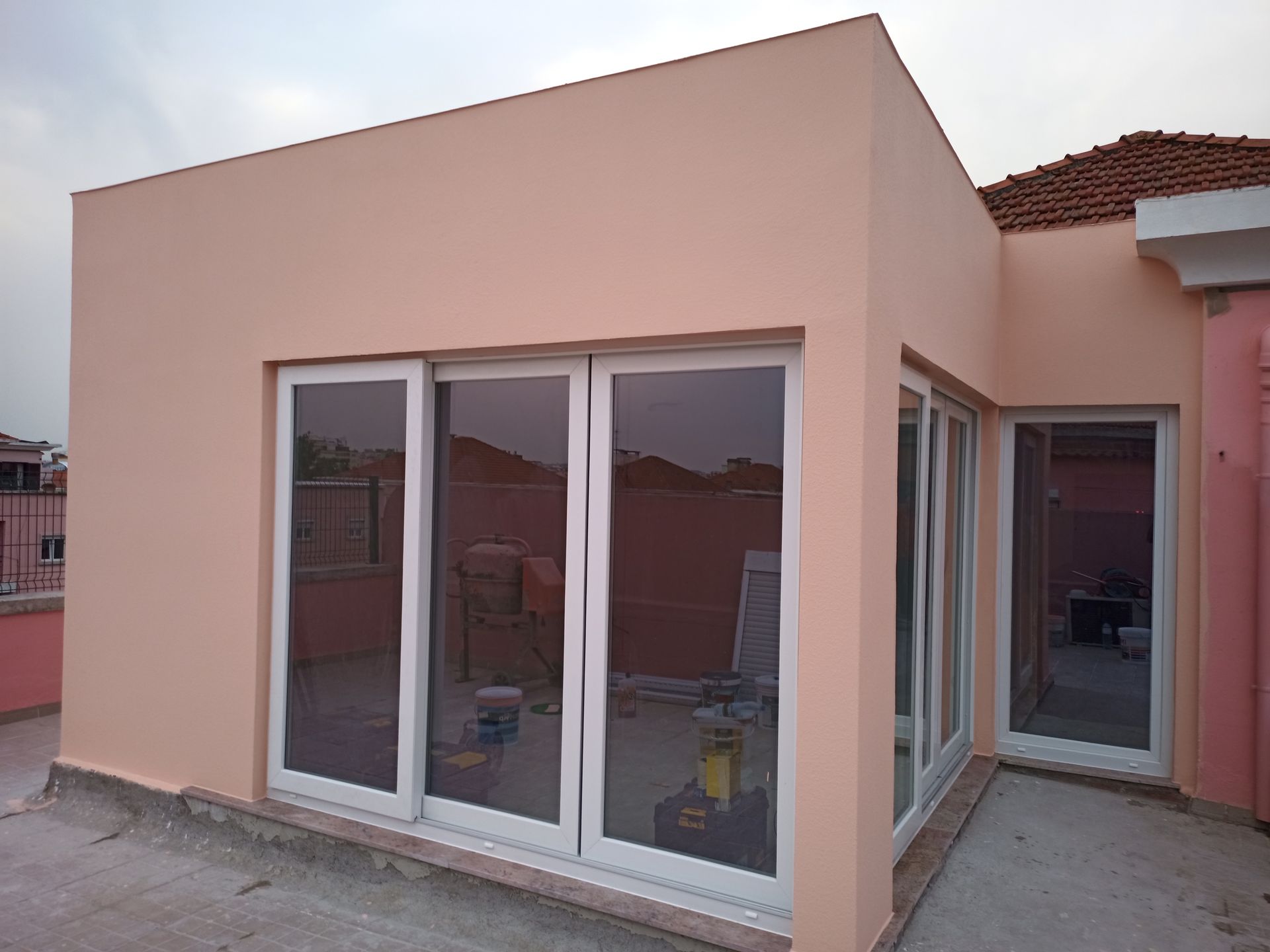 Prédio com portas de vidro deslizantes, pintado de cor pêssego claro, em um terraço na cobertura.