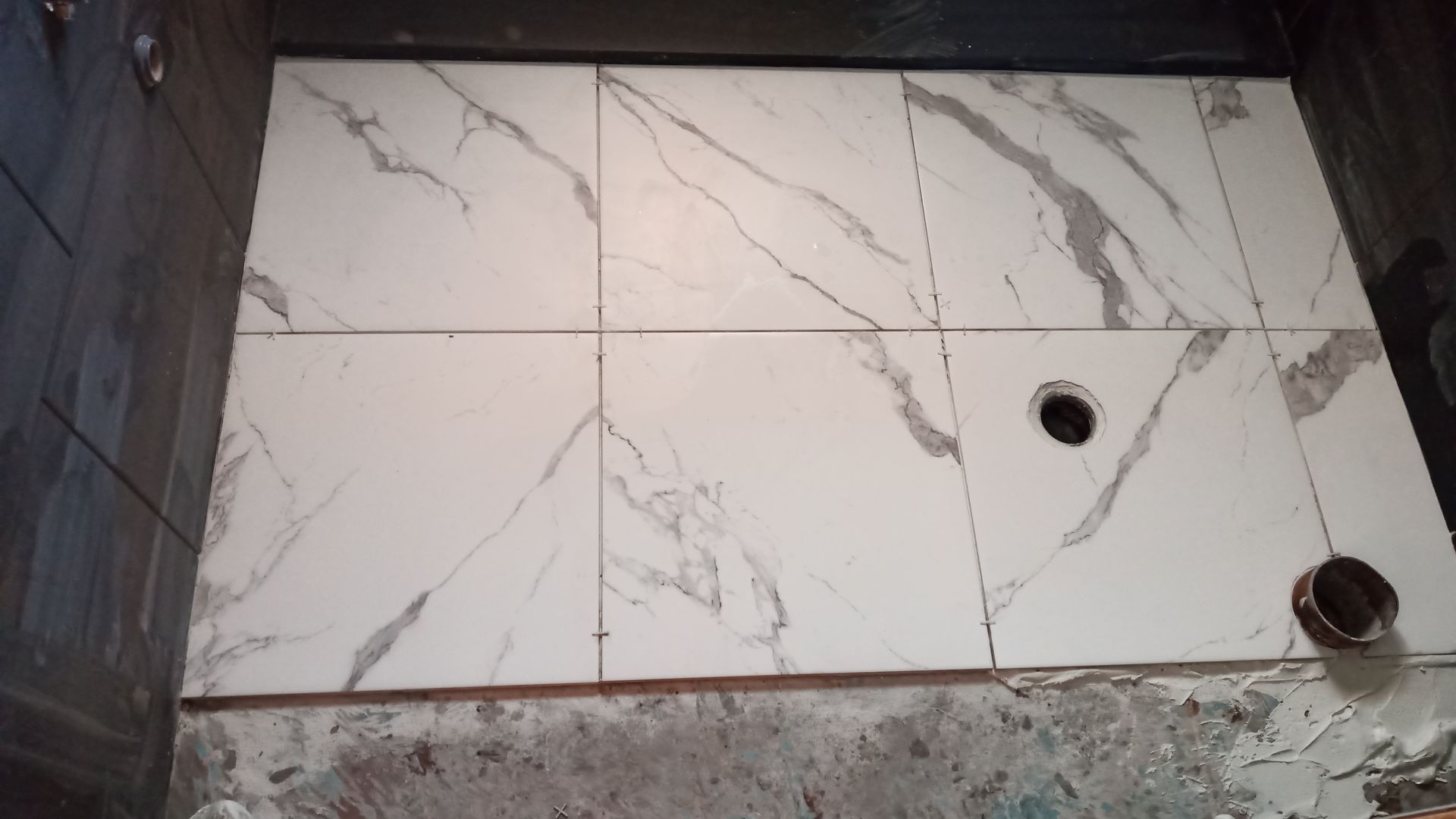 Piso do chuveiro revestido com azulejos de mármore branco, com ralo e cano visíveis, instalado em um banheiro.