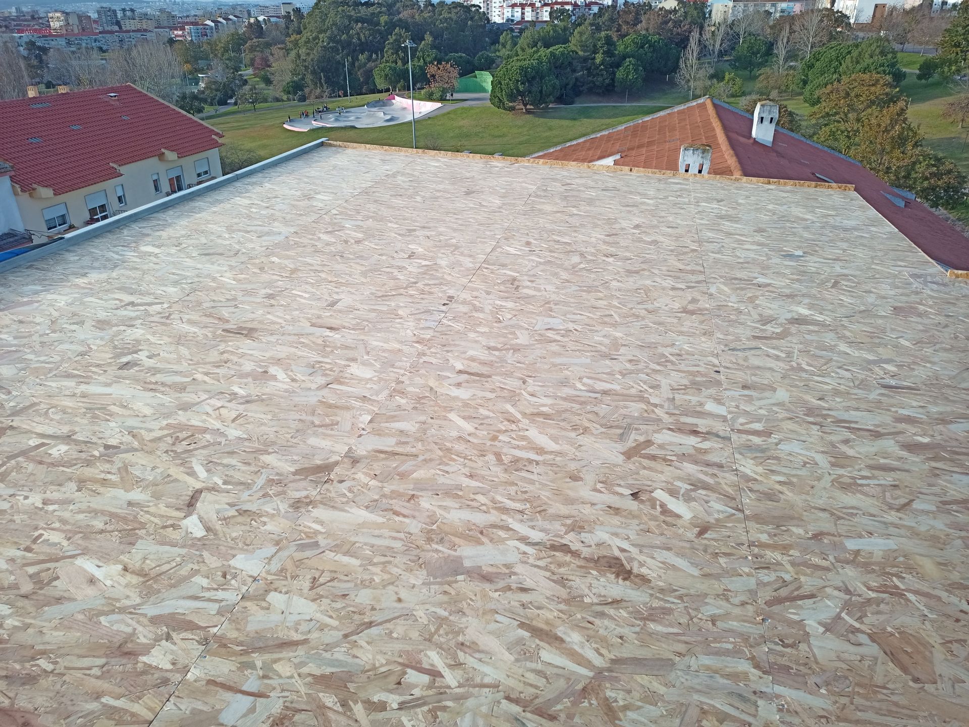 Laje de cobertura em OSB em um edifício, com telhado de telhas vermelhas visível ao fundo.