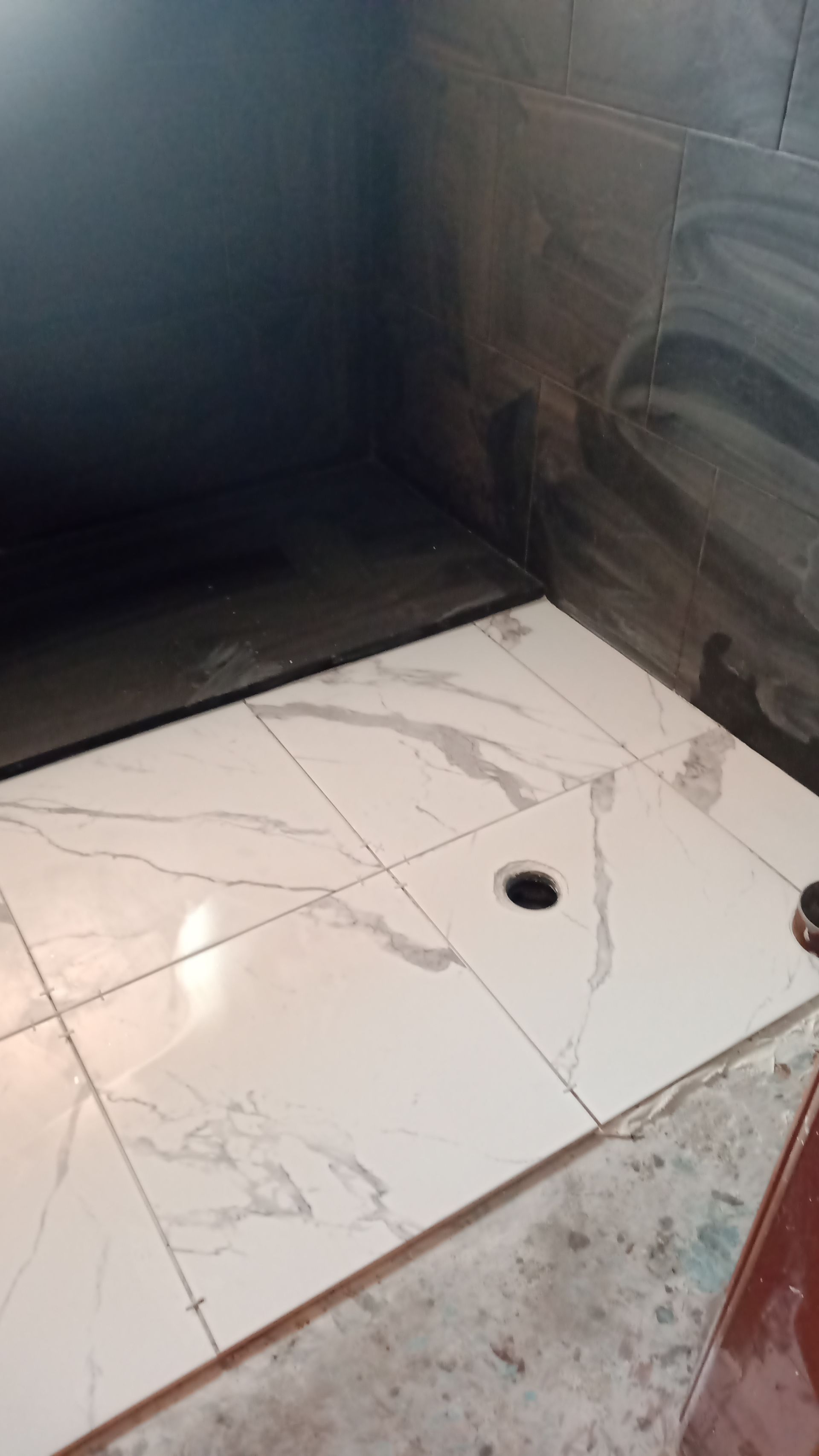 Piso de azulejos brancos com dois buracos, dentro de um recinto escuro.