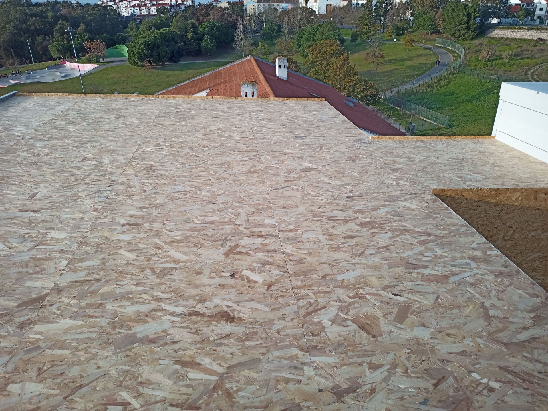 Vista aérea de um telhado de madeira OSB inacabado com uma paisagem residencial ao fundo.