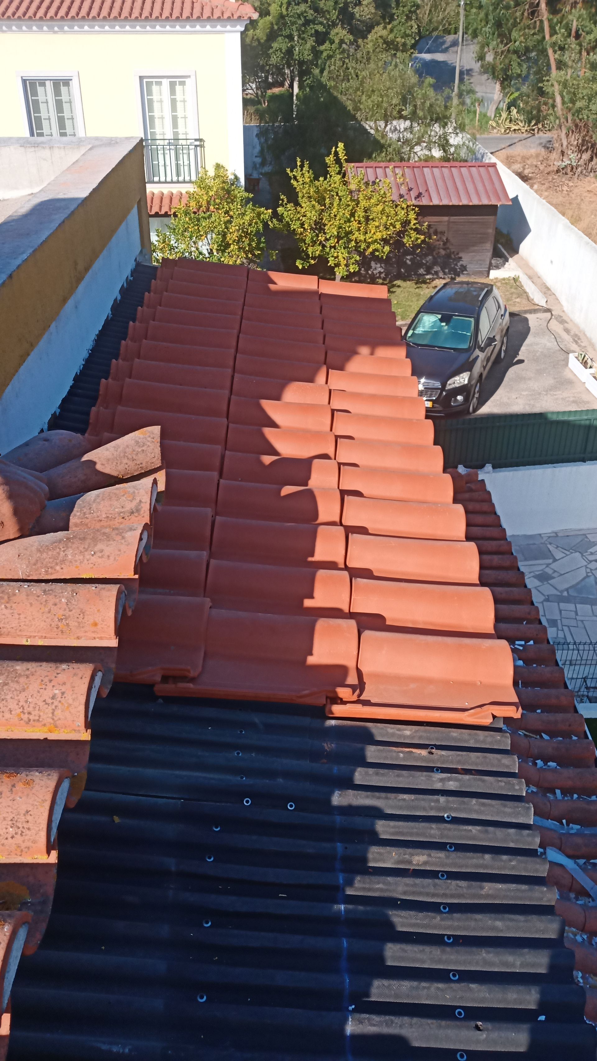 Telhado com telhas vermelhas sendo instaladas sobre uma subcobertura preta.