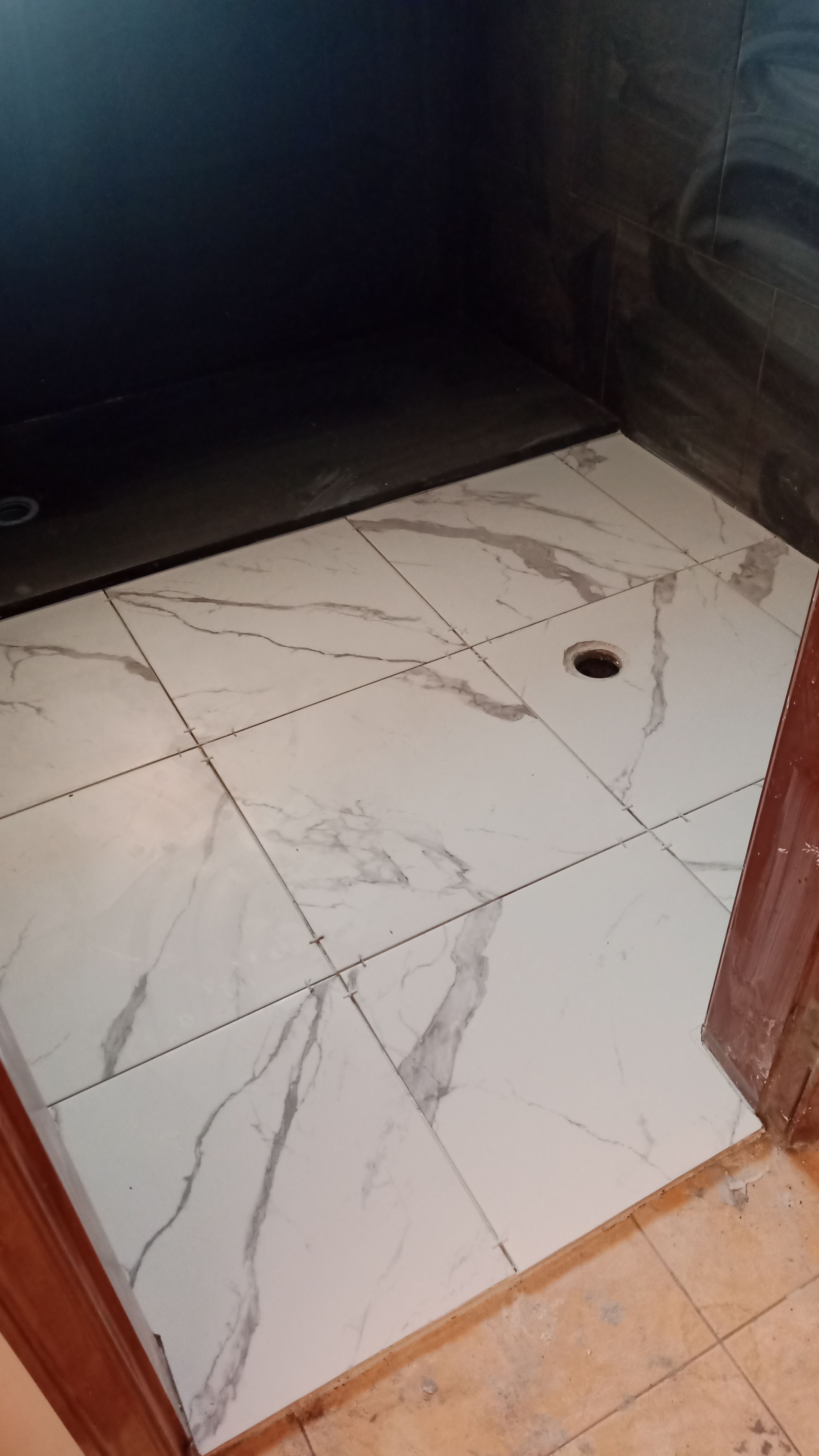 Box de chuveiro com azulejos brancos imitando mármore, ralo e paredes escuras.