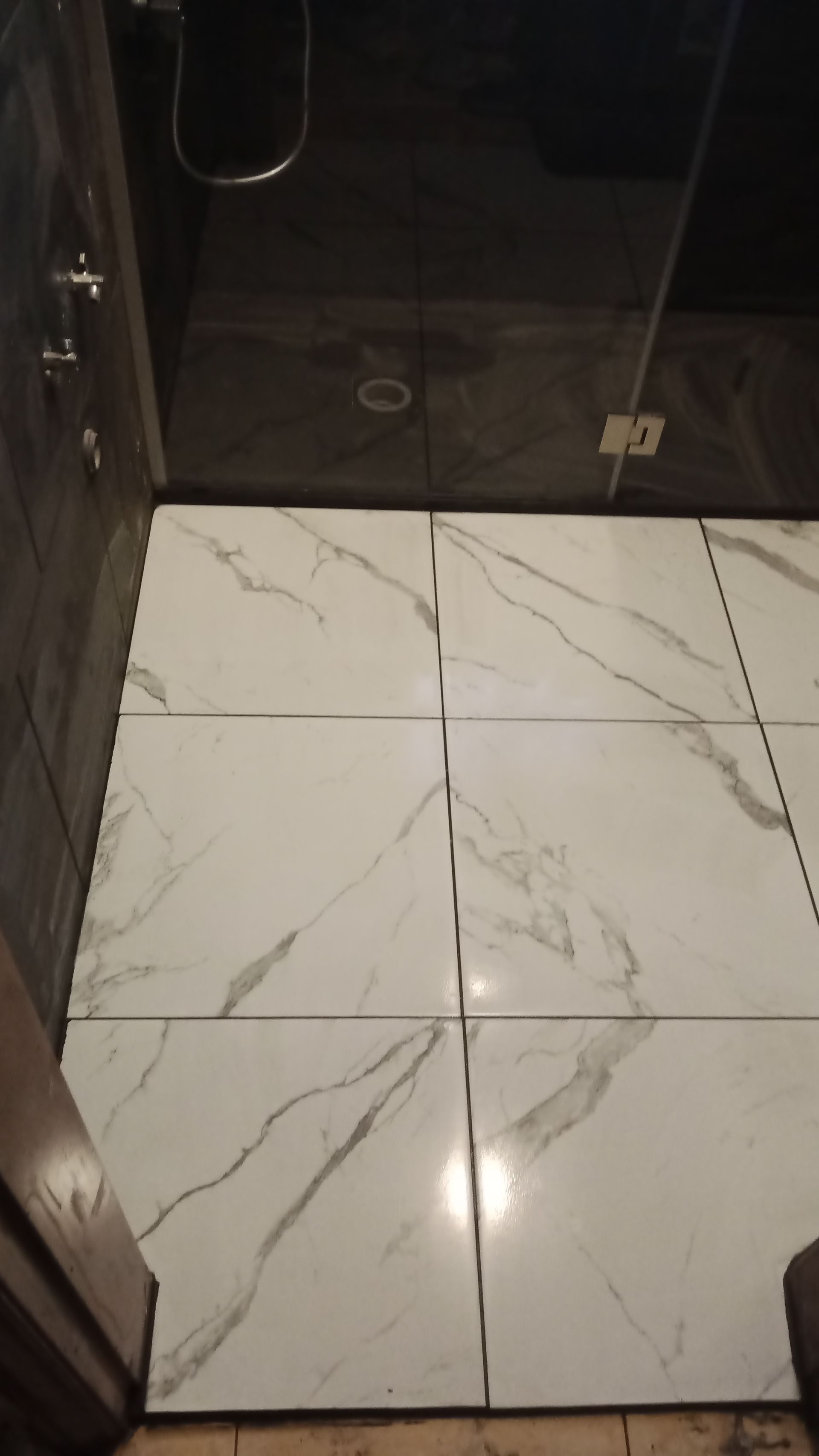 Piso do banheiro revestido com mármore branco, teto cinza escuro e chuveiro visível.