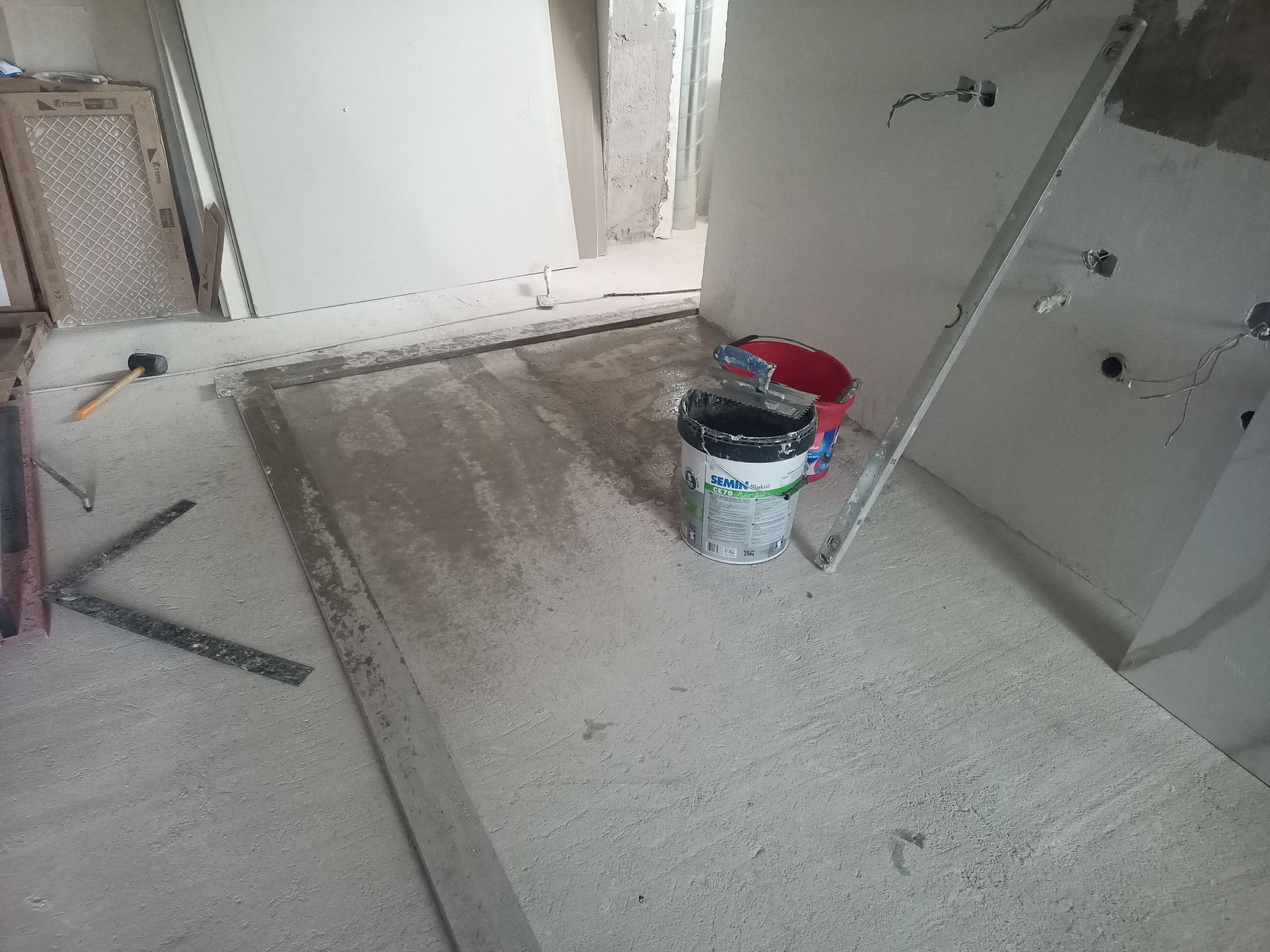 Canteiro de obras: piso de cimento, paredes, balde de tinta. Ferramentas e entulho espalhados por toda parte.