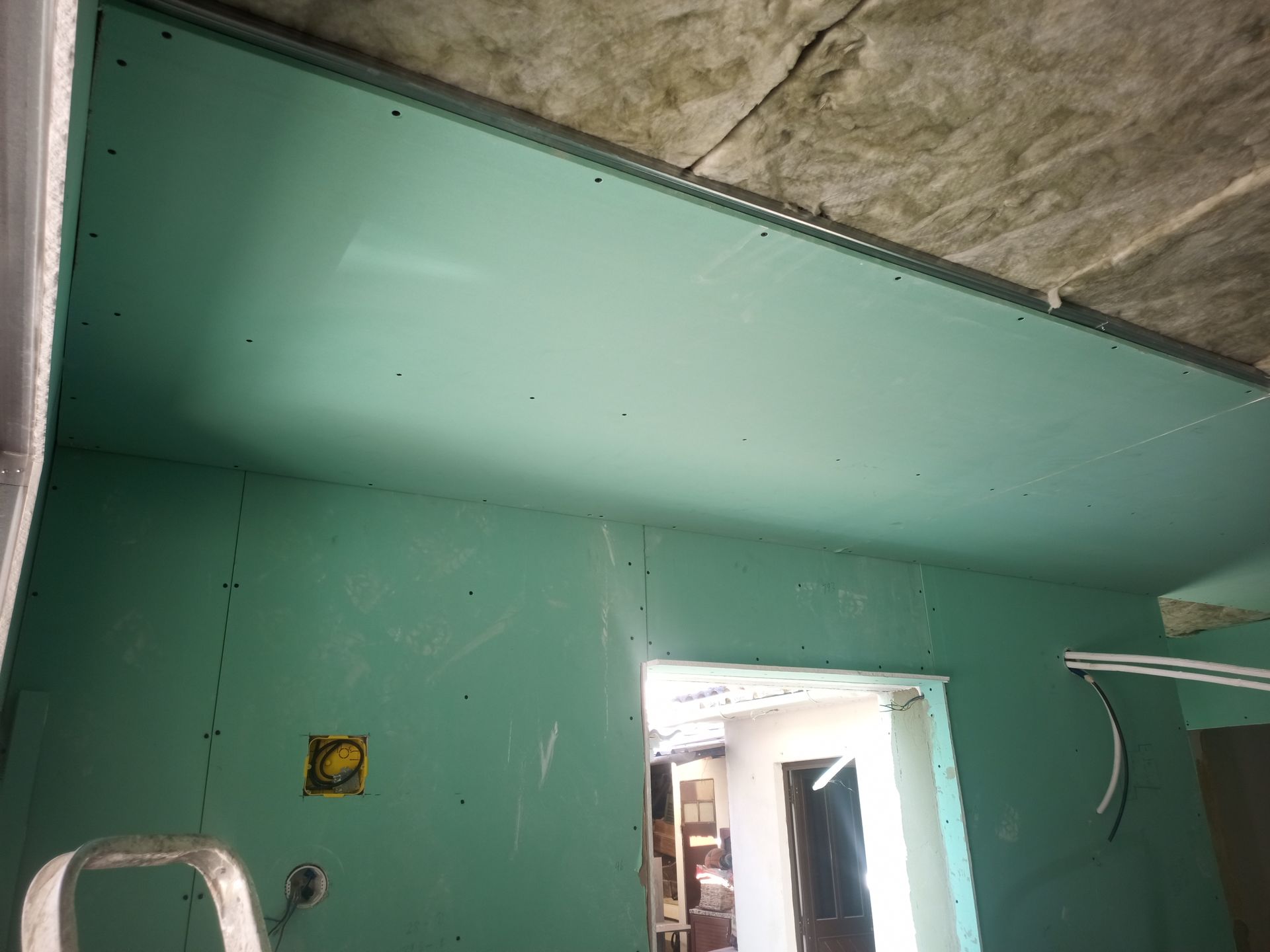 Vista interna de um cômodo em construção com drywall verde nas paredes e no teto.