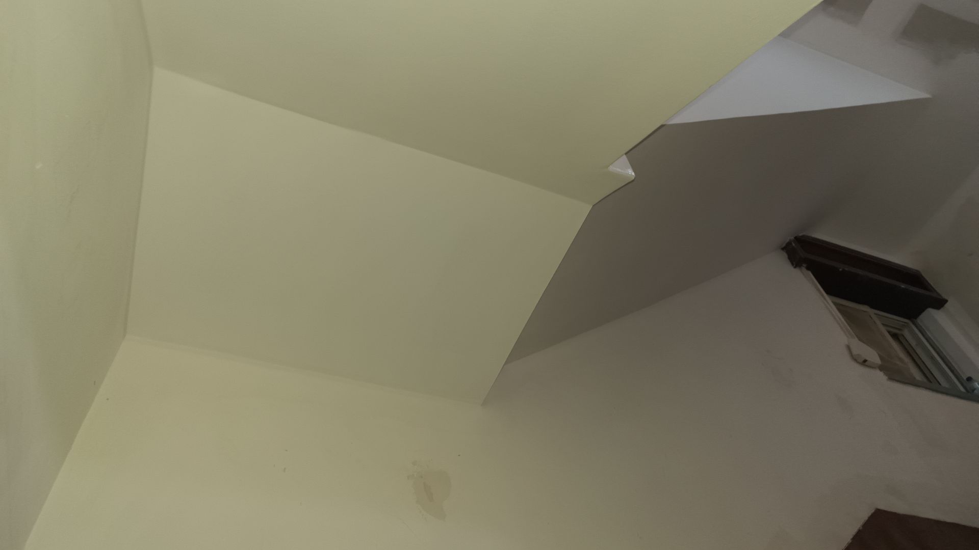 Vista em ângulo baixo de um teto claro com uma seção rasgada revelando um espaço mais escuro; uma janela é visível.