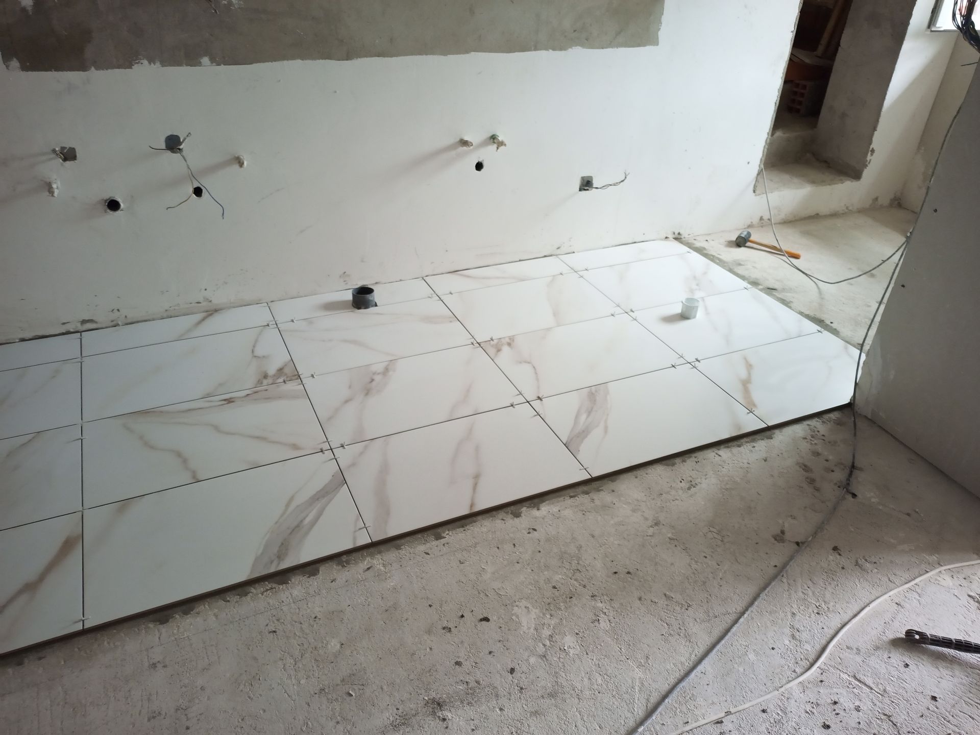 Interior em construção, mostrando o piso parcialmente revestido com azulejos. Azulejos brancos com efeito mármore, dispostos em padrão quadriculado.