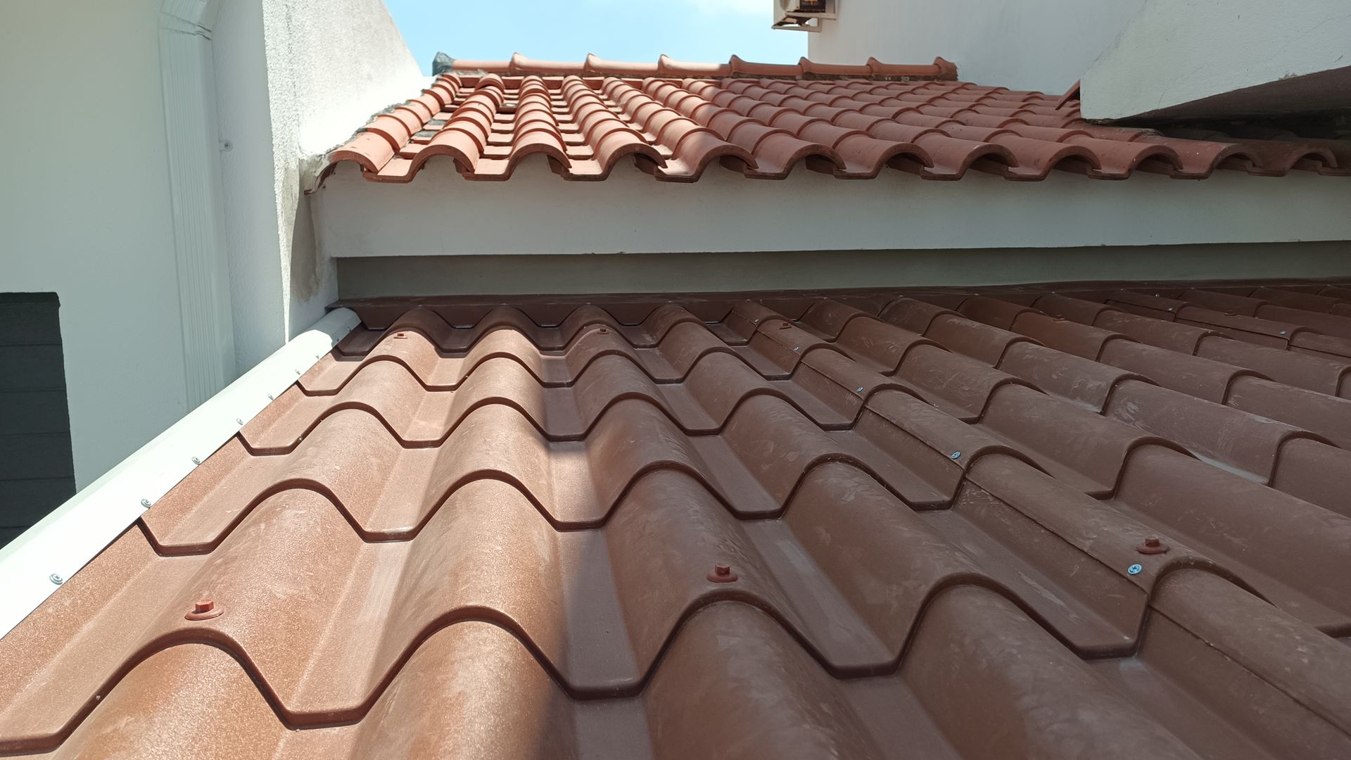 Telhado de telhas de barro vermelho visto de baixo, contra uma parede branca e céu azul.