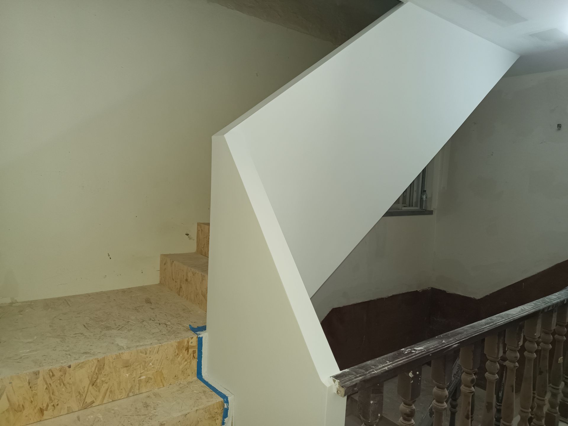 Escadaria com degraus de pedra, paredes brancas e corrimão de madeira.