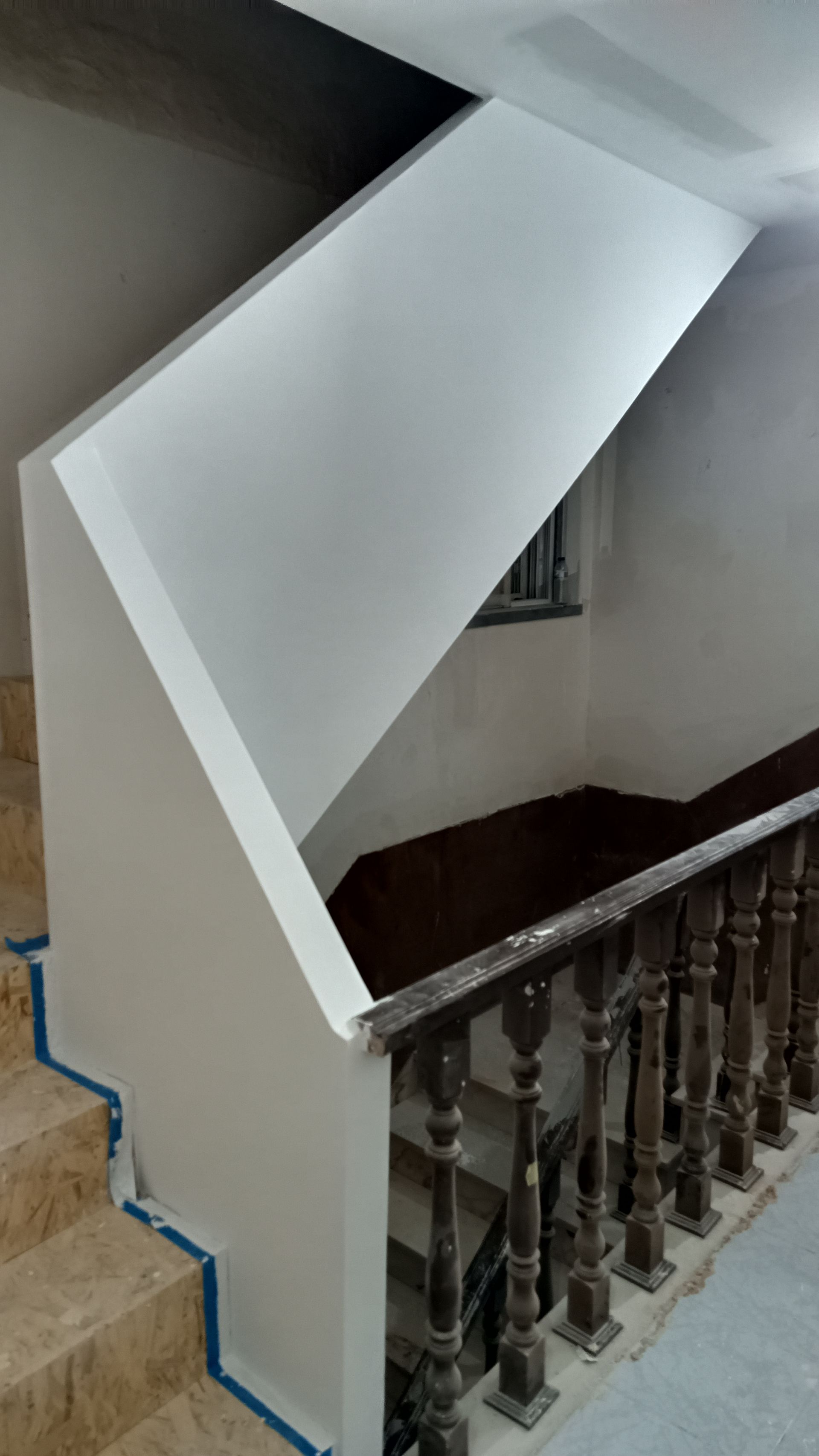 Escada com paredes claras e corrimão de madeira escura. Fita azul protege as bordas dos degraus.