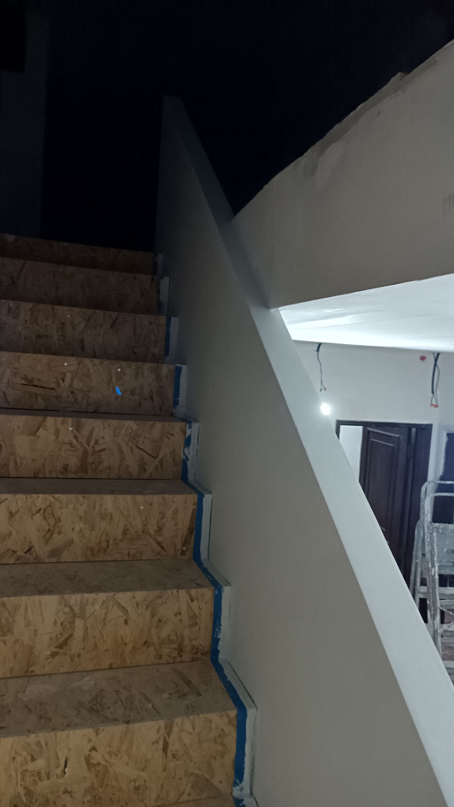 Escadaria de pedra subindo ao lado de uma parede branca. Os degraus têm bordas azuis. Interior pouco iluminado.