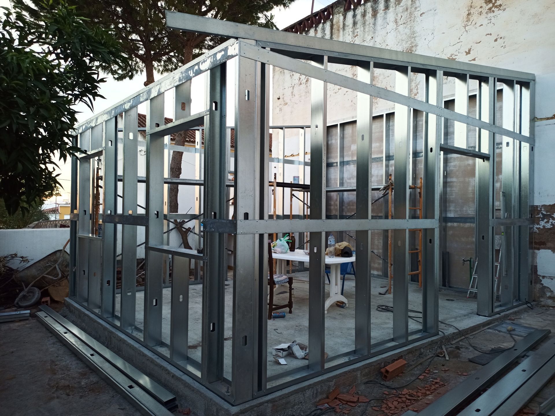 Estrutura metálica para paredes e telhado de um edifício, em área externa. Canteiro de obras com vigas expostas.