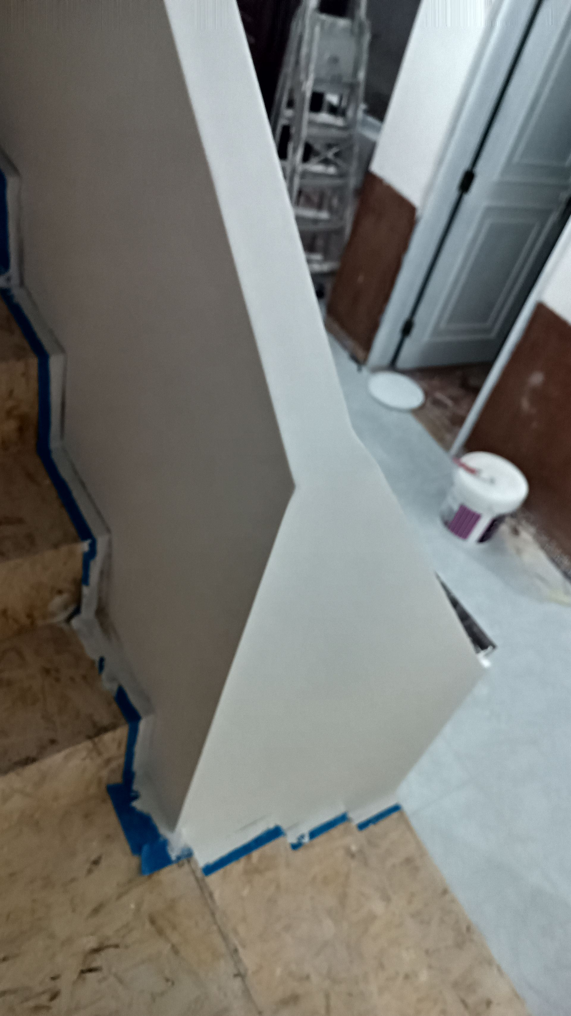 Escada com parede pintada de branco, fita adesiva azul para pintura e degraus de mármore, ambiente interno.