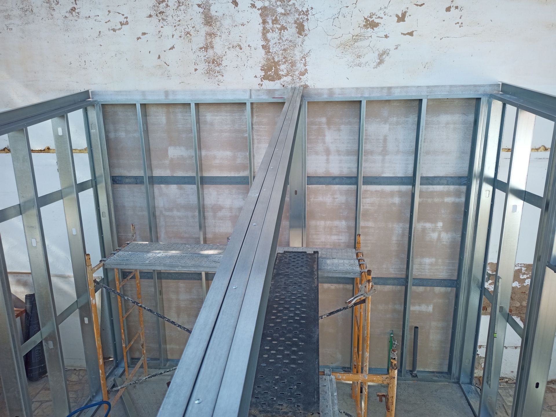 Estrutura metálica de uma sala em construção com andaimes visíveis.