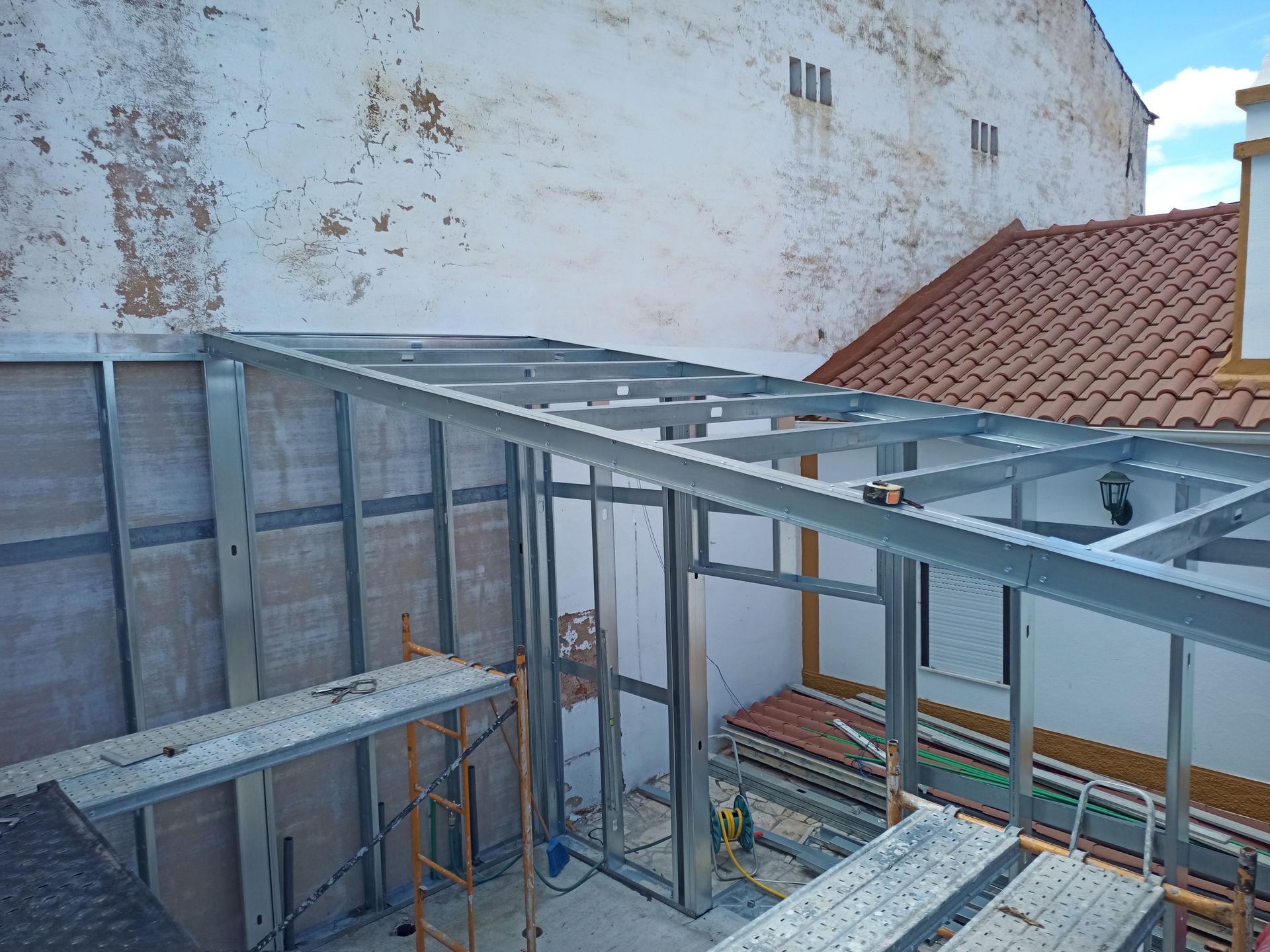 Estrutura metálica de uma passarela coberta anexa a um edifício, com andaimes e fachadas do prédio visíveis.