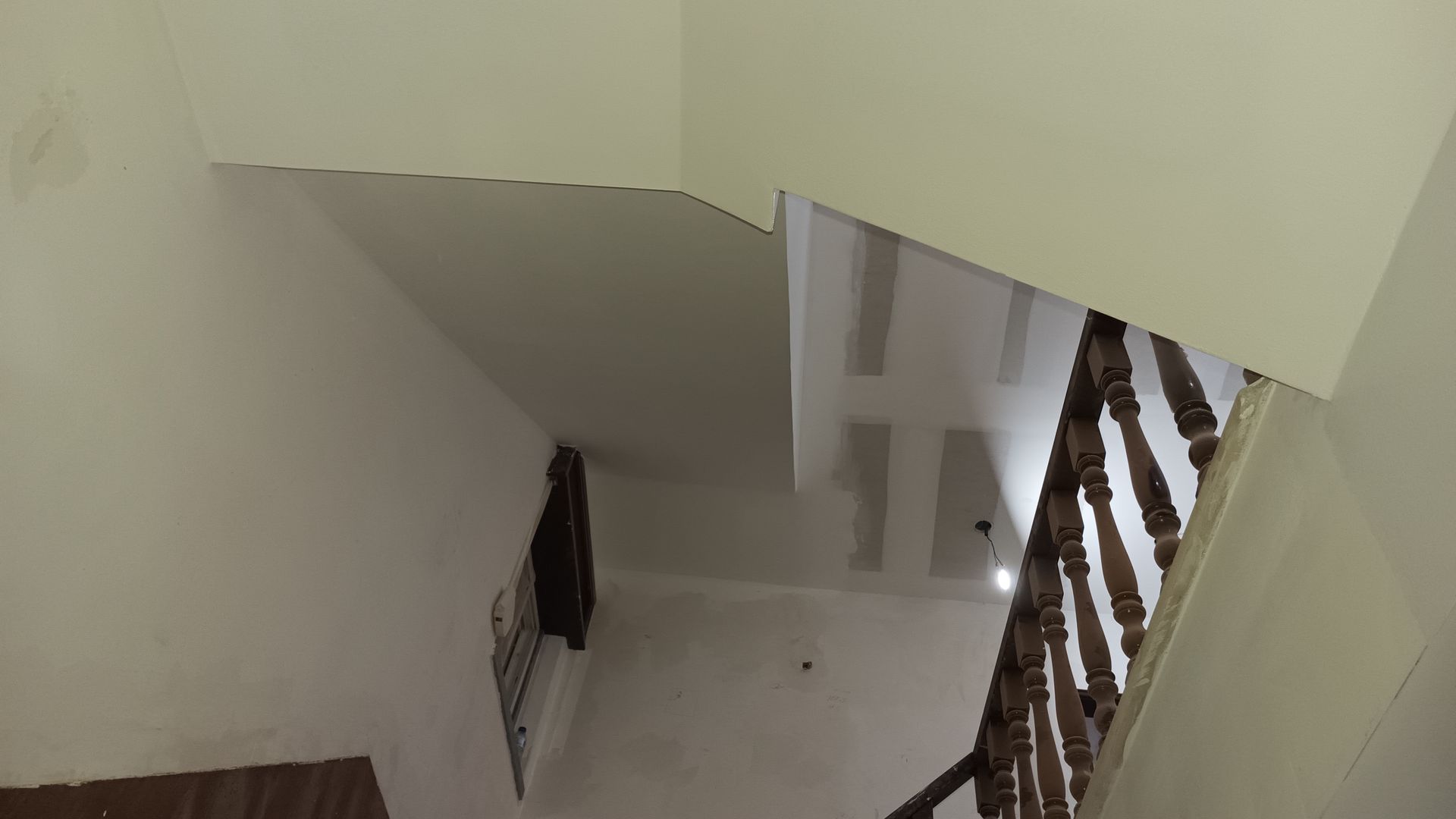 Vista de uma escadaria de paredes brancas com corrimão de madeira e roupas escuras penduradas.