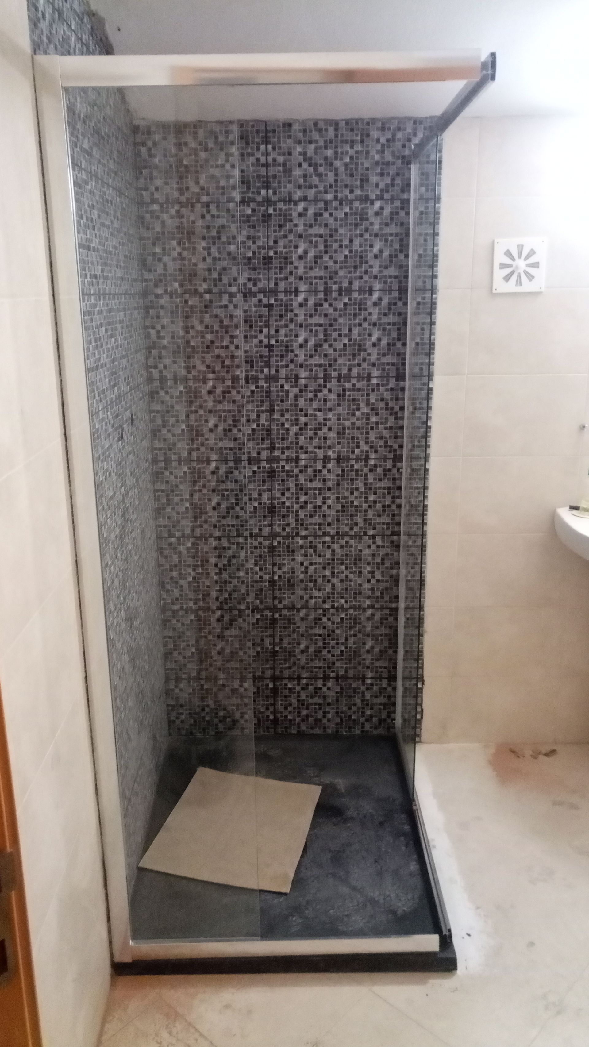 Cabine de duche com paredes de vidro e interior revestido a azulejos pretos.