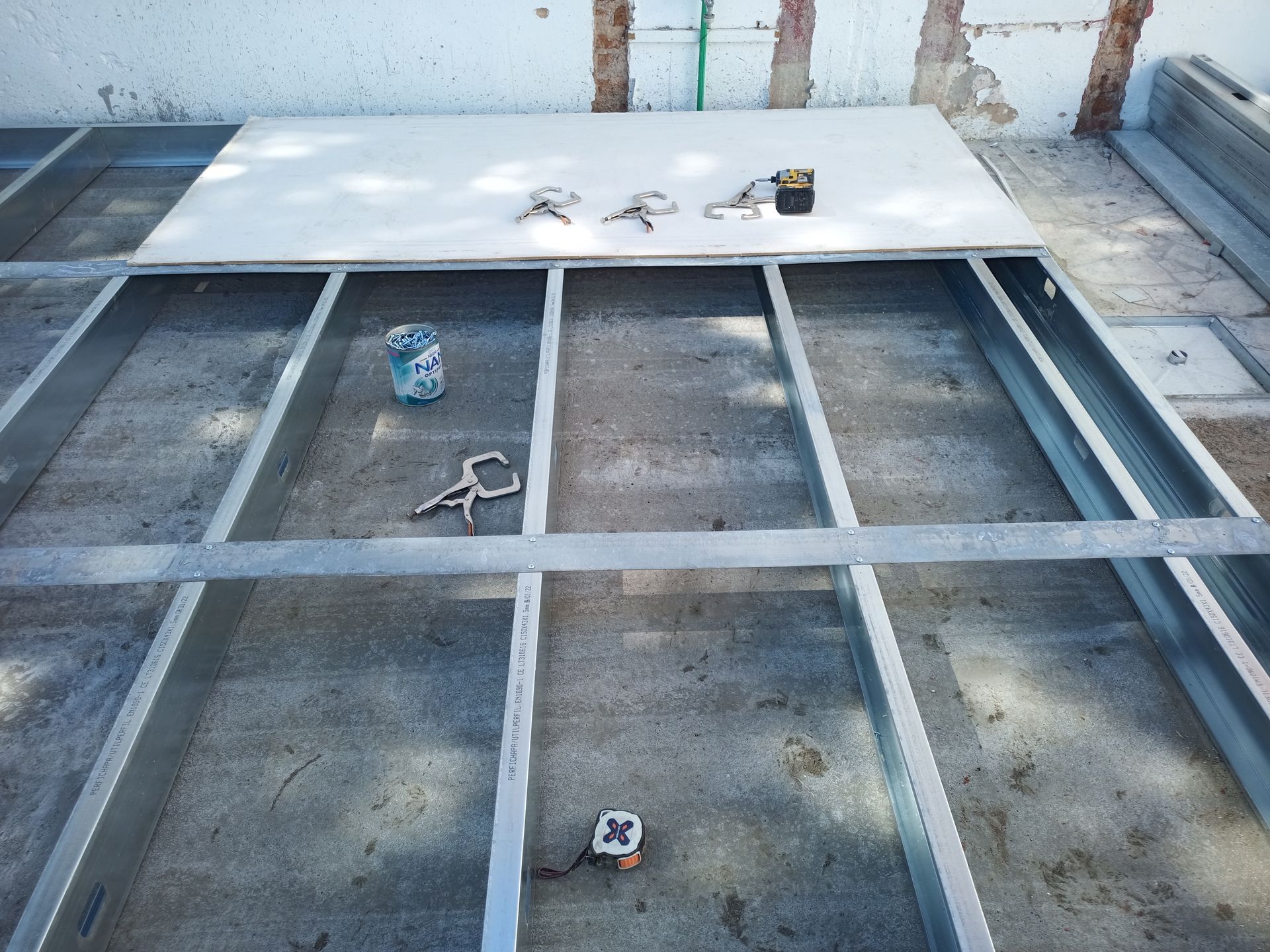 Estrutura de aço com drywall, ferramentas e piso de concreto, provavelmente construção ao ar livre.