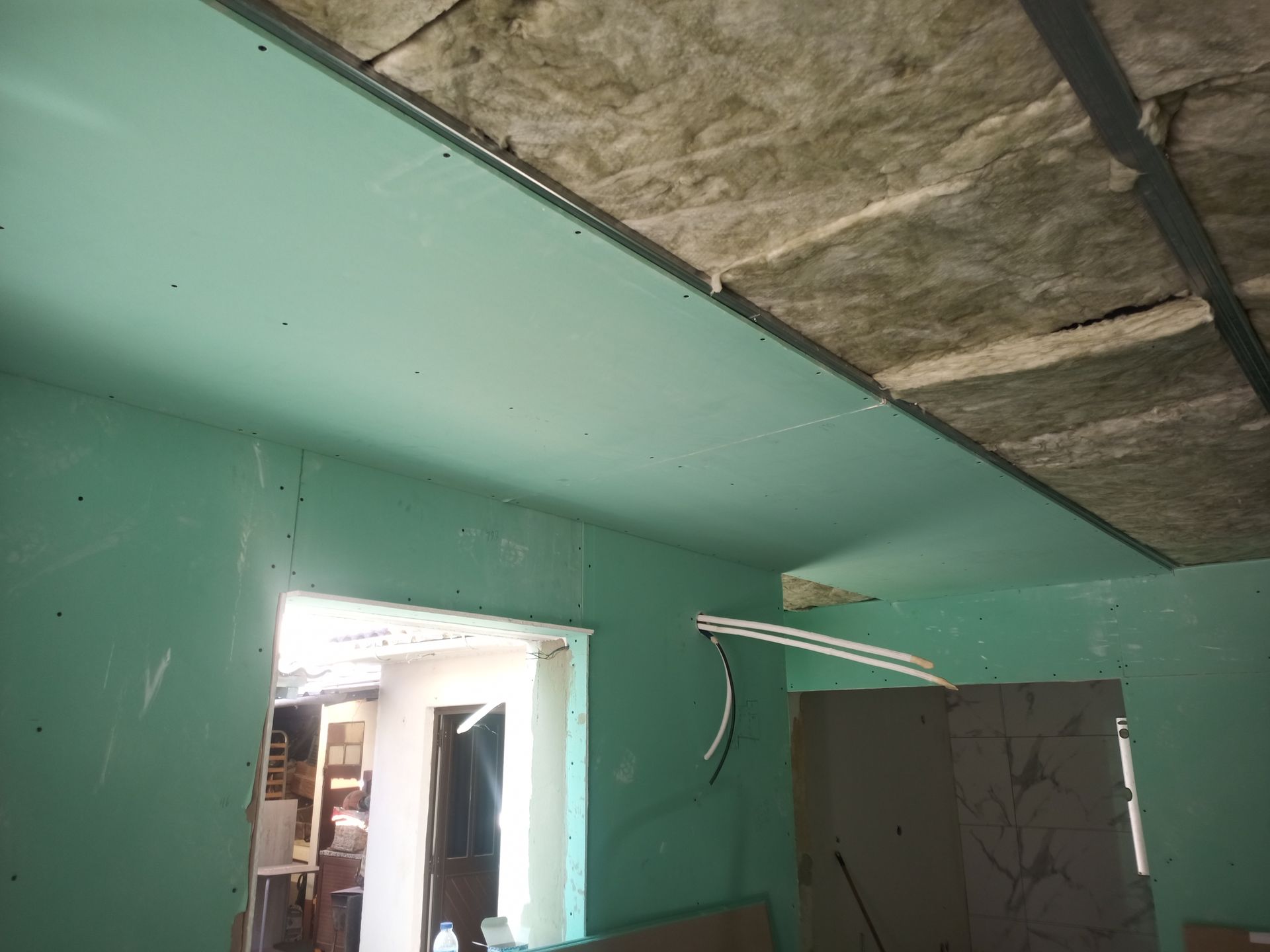 Interior de um cômodo em construção, com drywall verde nas paredes e no teto.