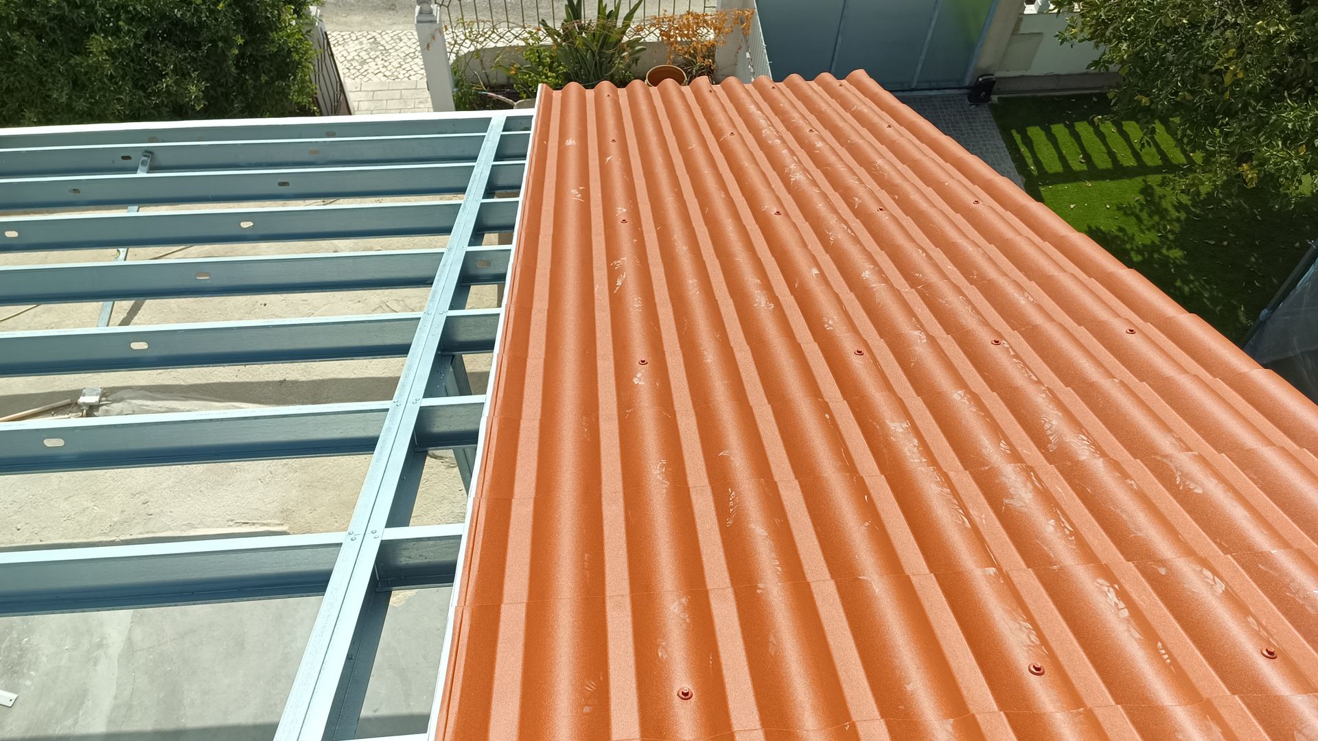 Telhado ondulado laranja sendo instalado em uma estrutura metálica, na área externa.