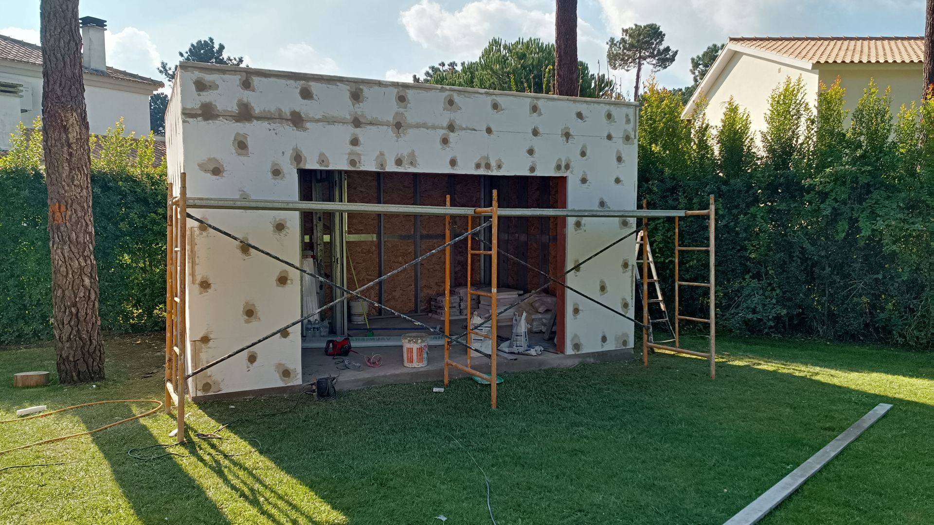 Um pequeno edifício em construção, coberto com isolamento térmico, com andaimes em um pátio gramado.