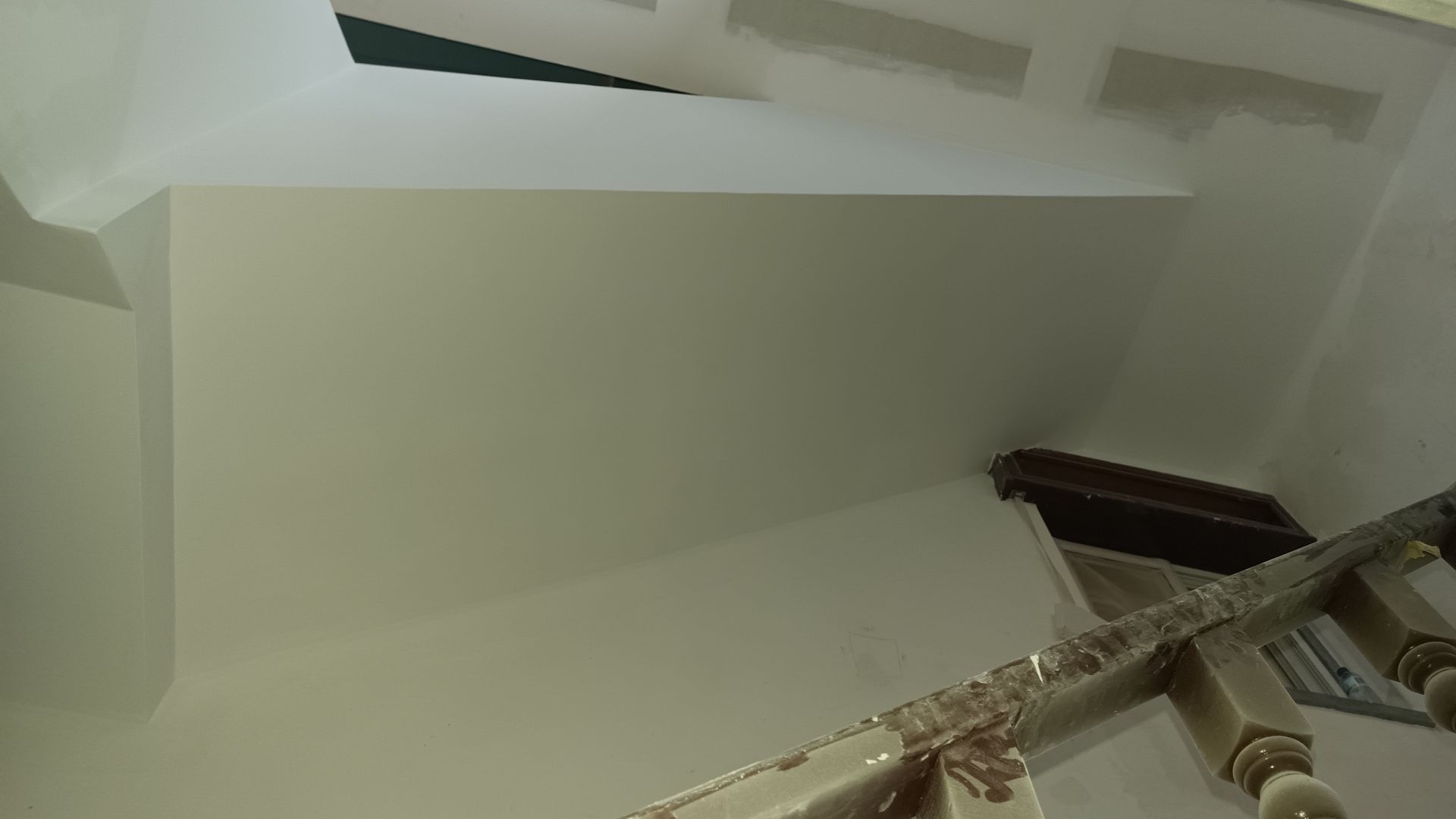 Escadaria com paredes brancas e corrimão de madeira, vista de baixo.