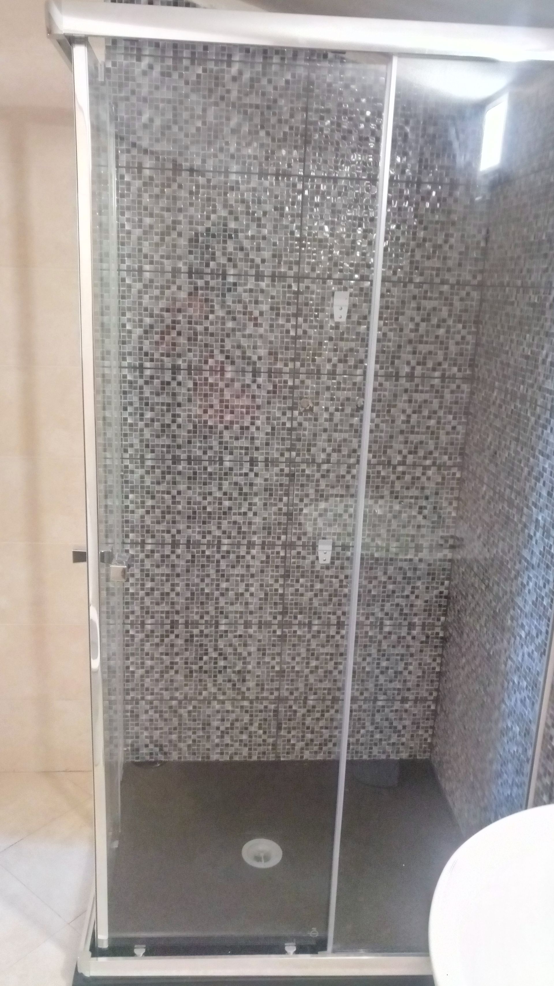 Cabine de duche com portas de vidro deslizantes e painel de azulejos em mosaico.