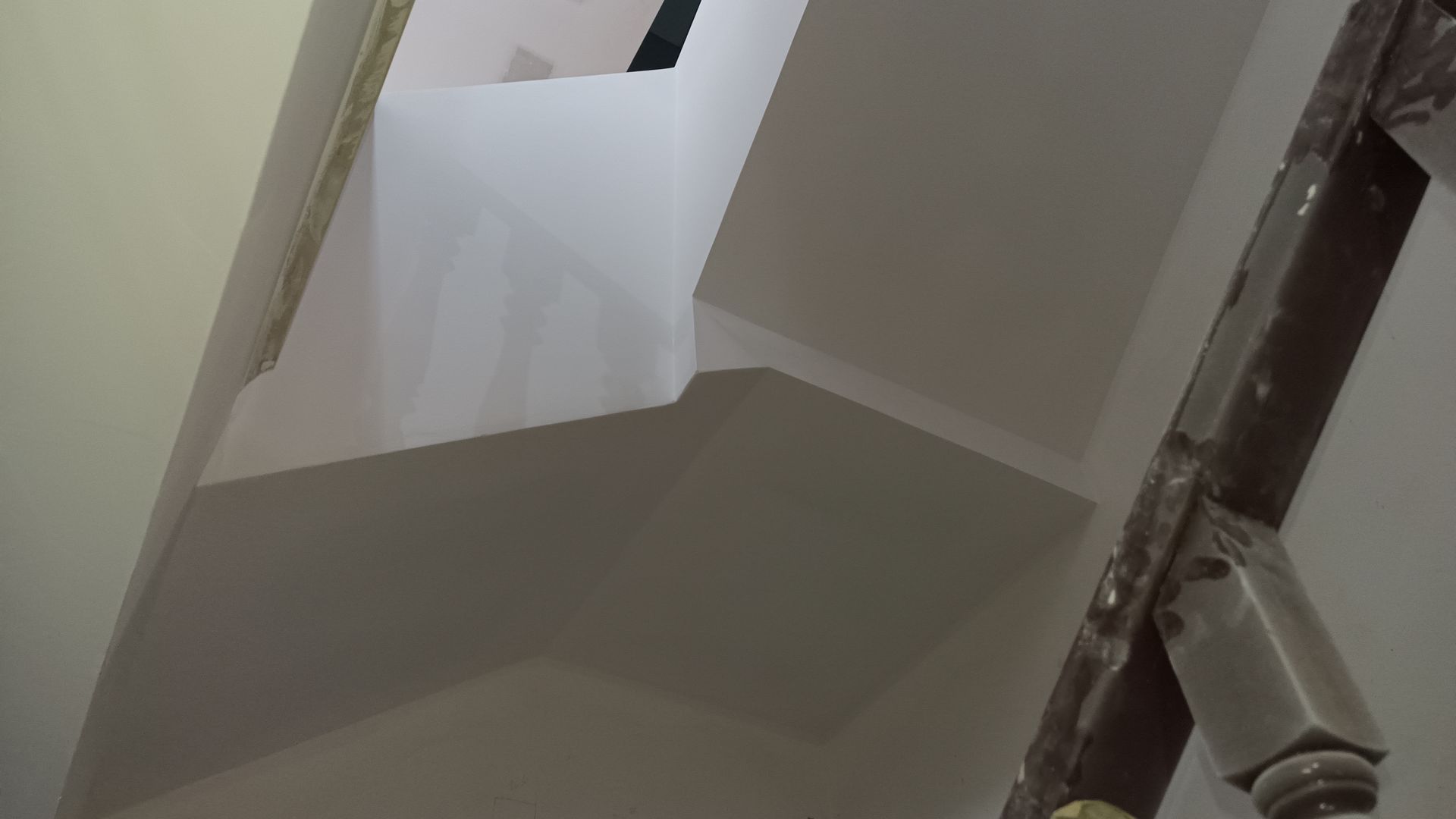 Escada com paredes brancas e corrimão de madeira marrom.