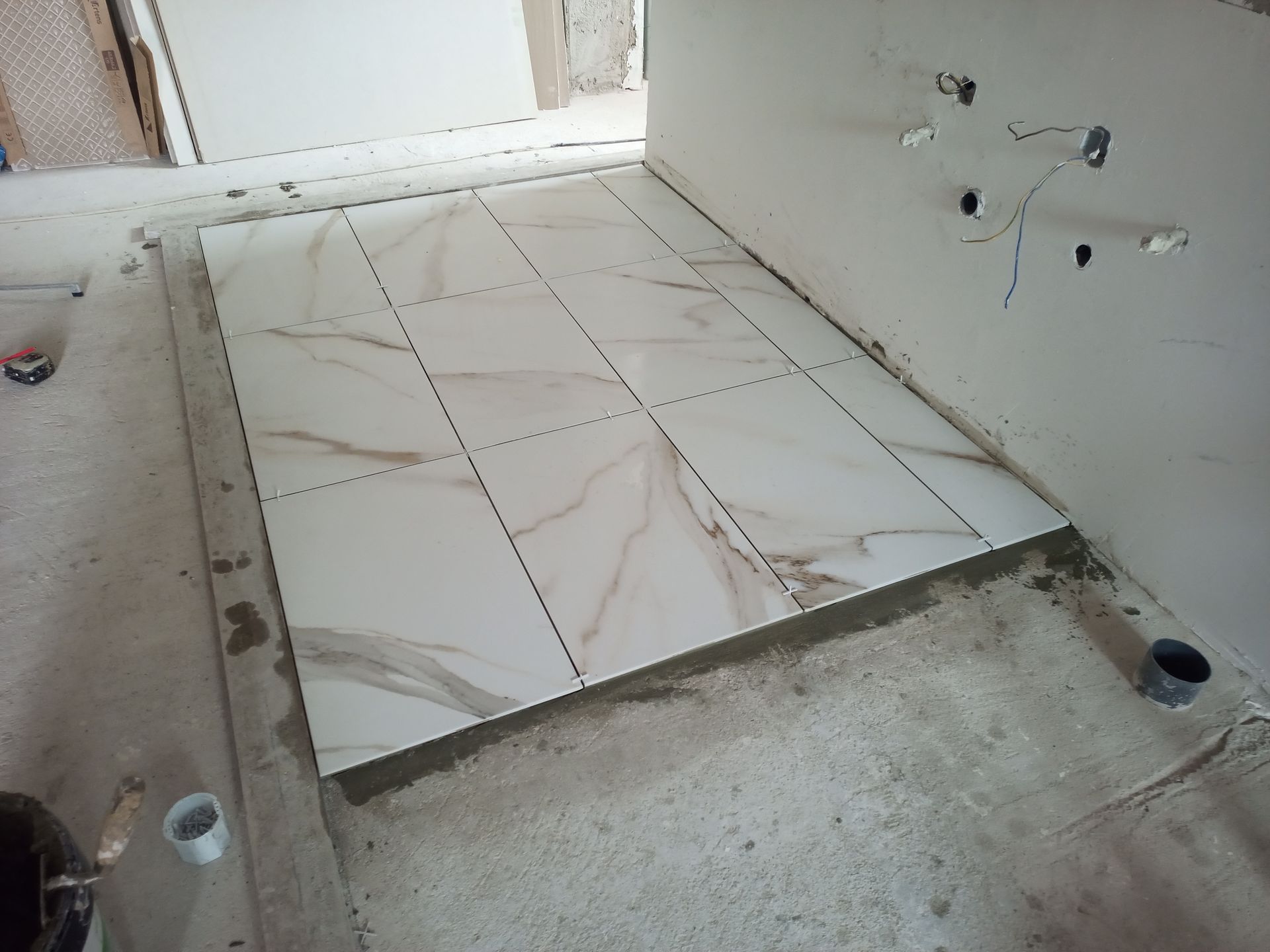 Instalação de azulejos no piso do banheiro em andamento; grandes azulejos retangulares com padrão semelhante a mármore assentados sobre concreto.