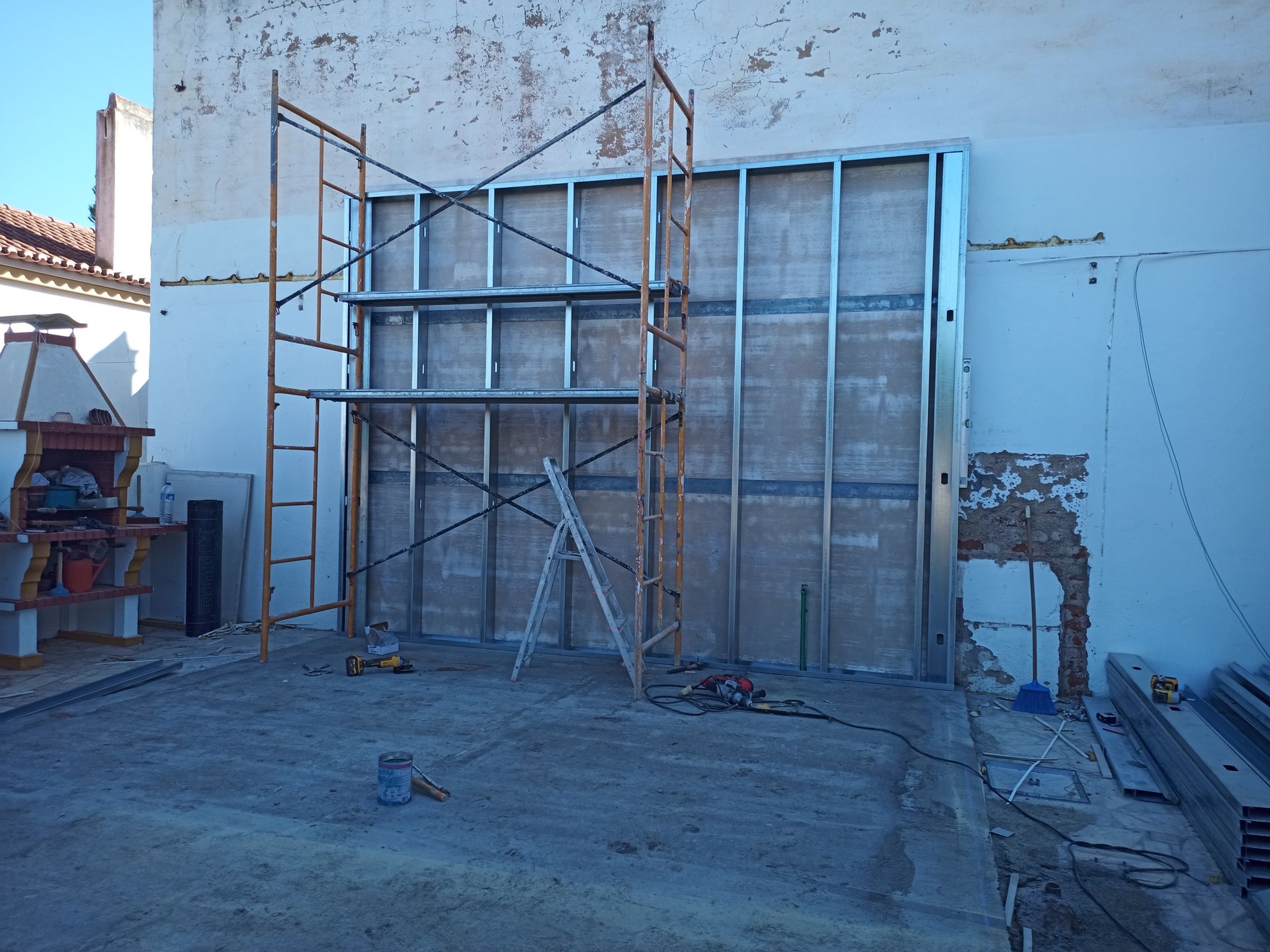 Parede com estrutura metálica em construção, com andaimes montados contra uma fachada desgastada.