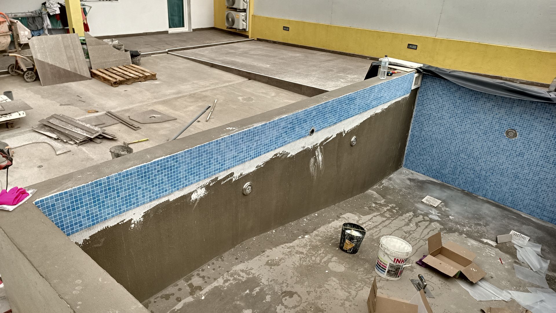 Piscina em construção com azulejos azuis, paredes marrons e piso de concreto.