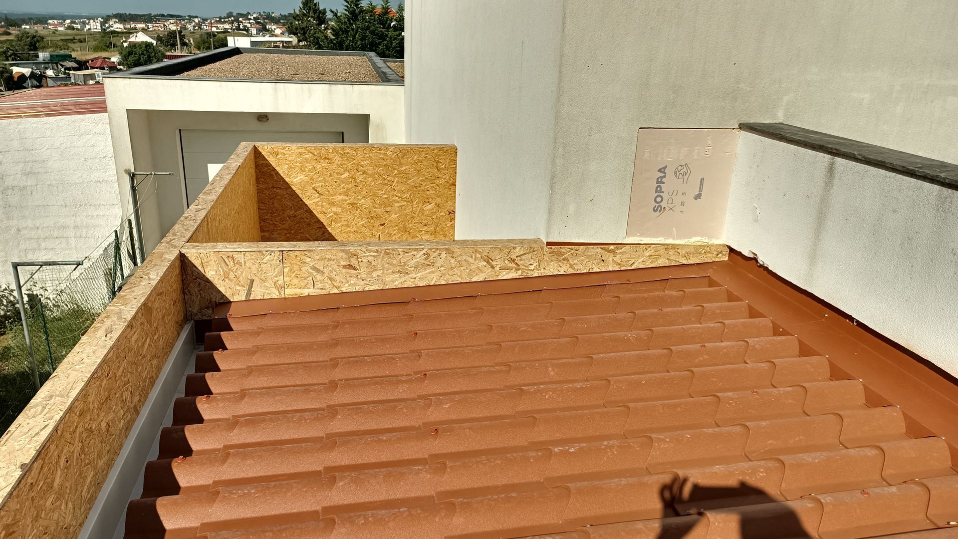 Telhado de telhas de terracota com barreira de madeira, contra uma parede branca com vista para a cidade.