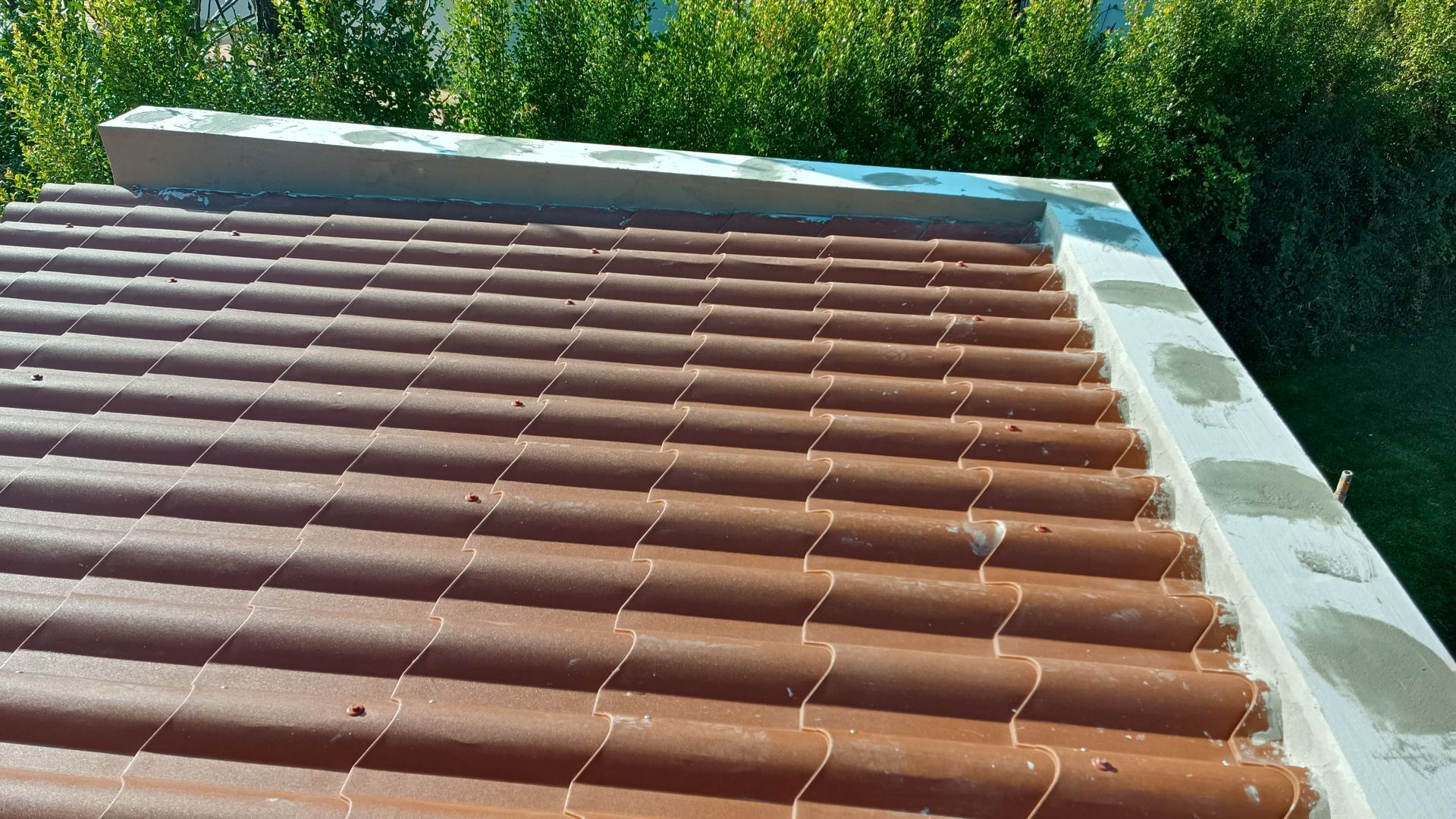 Telhado de telha marrom com borda de concreto, fundo de folhagem verde.