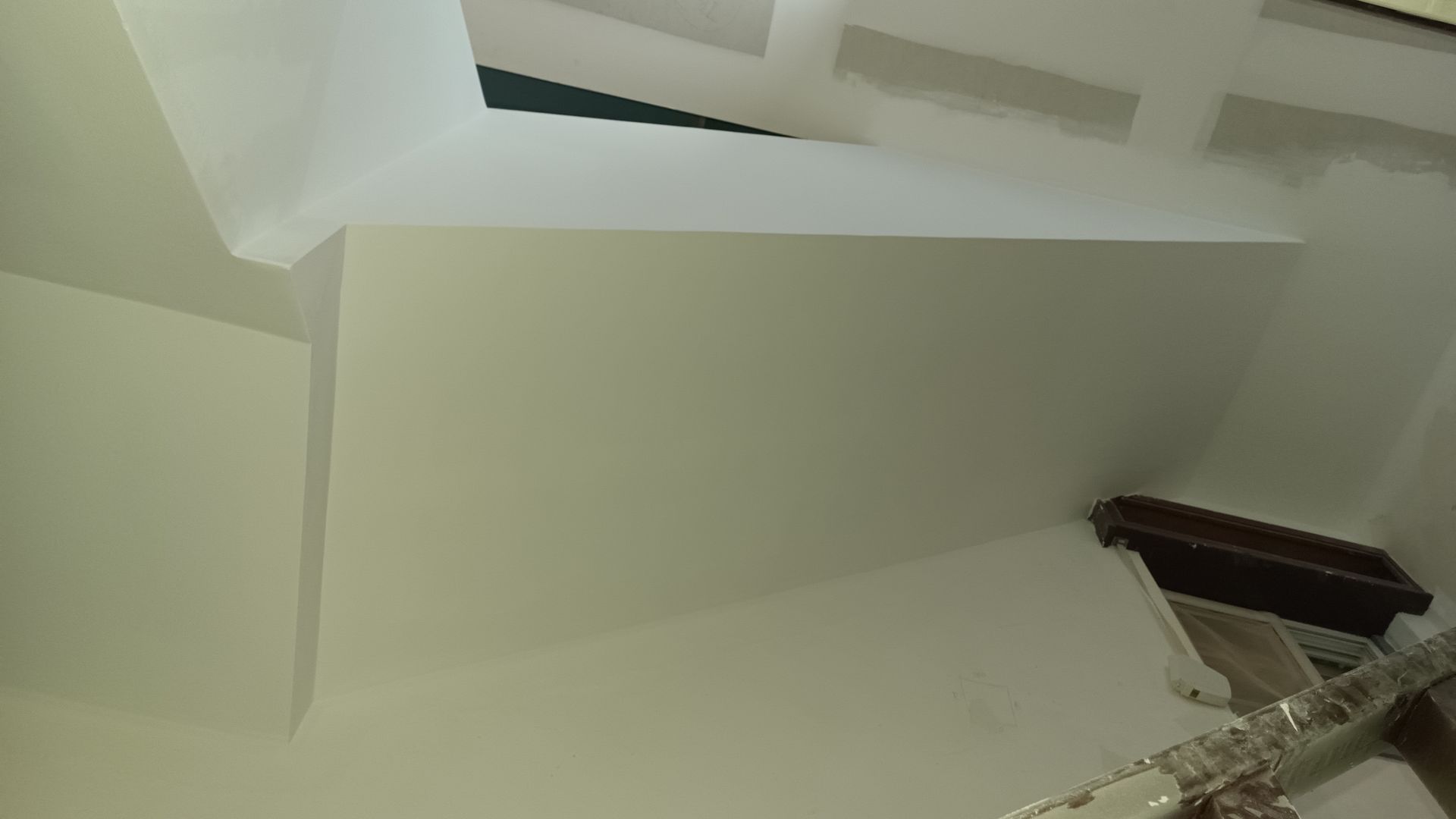 Detalhes arquitetônicos internos pintados de branco. Uma viga é visível, assim como partes das paredes e do teto.