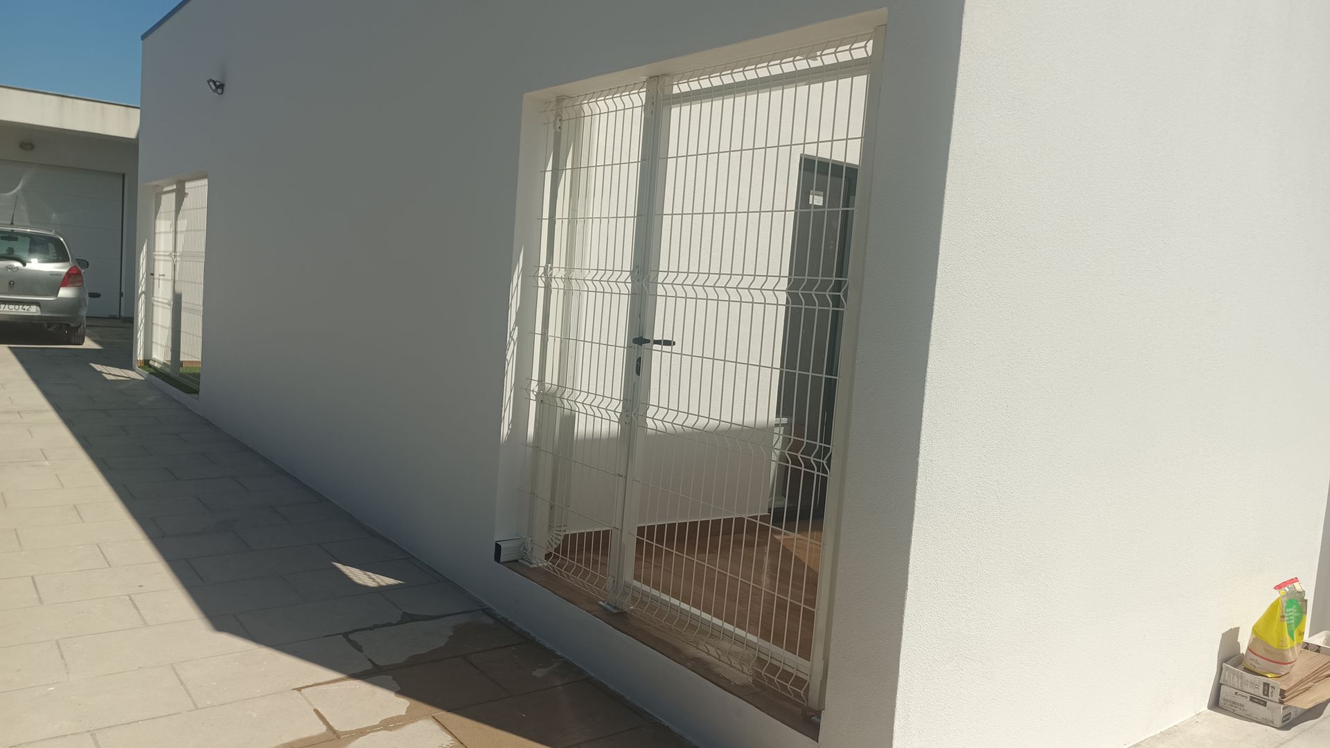 Fachada branca de um prédio com uma janela e um carro estacionado na entrada da garagem.