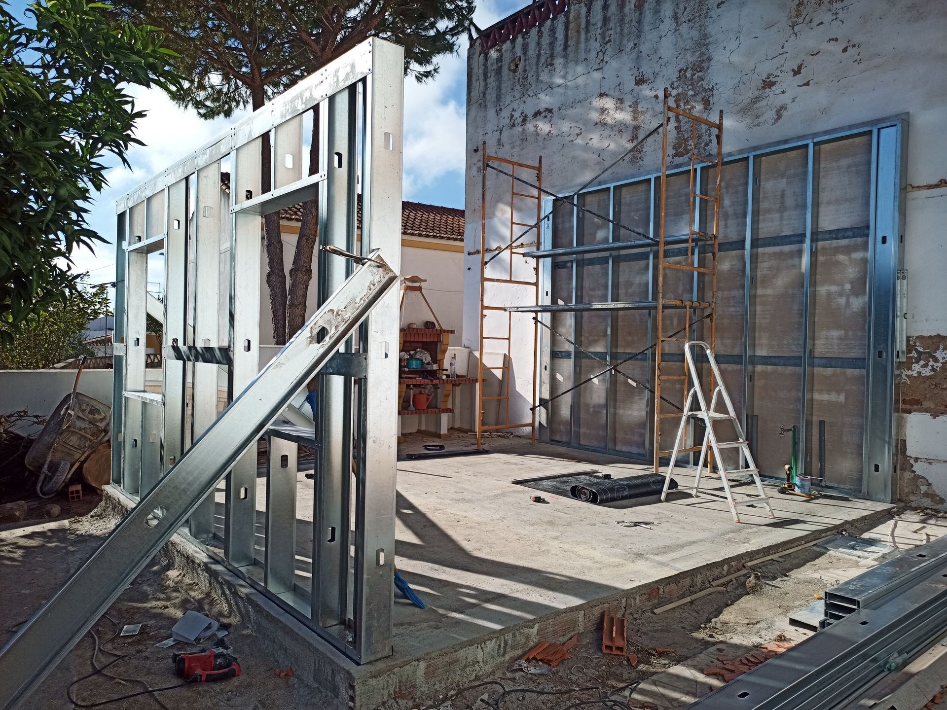 Estrutura metálica da parede de um edifício em construção, com uma janela e uma escada visíveis.