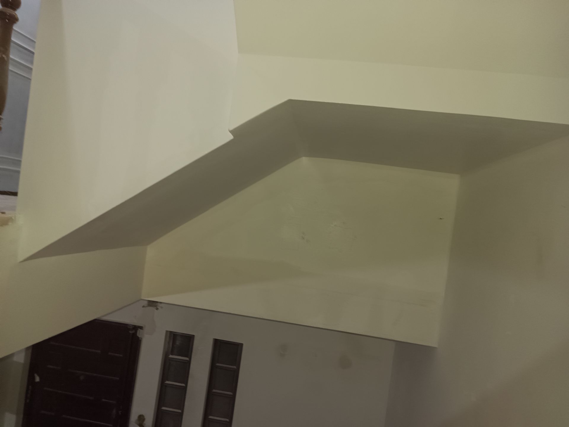 Corredor pintado de bege com uma escada no andar superior, visto de cima.