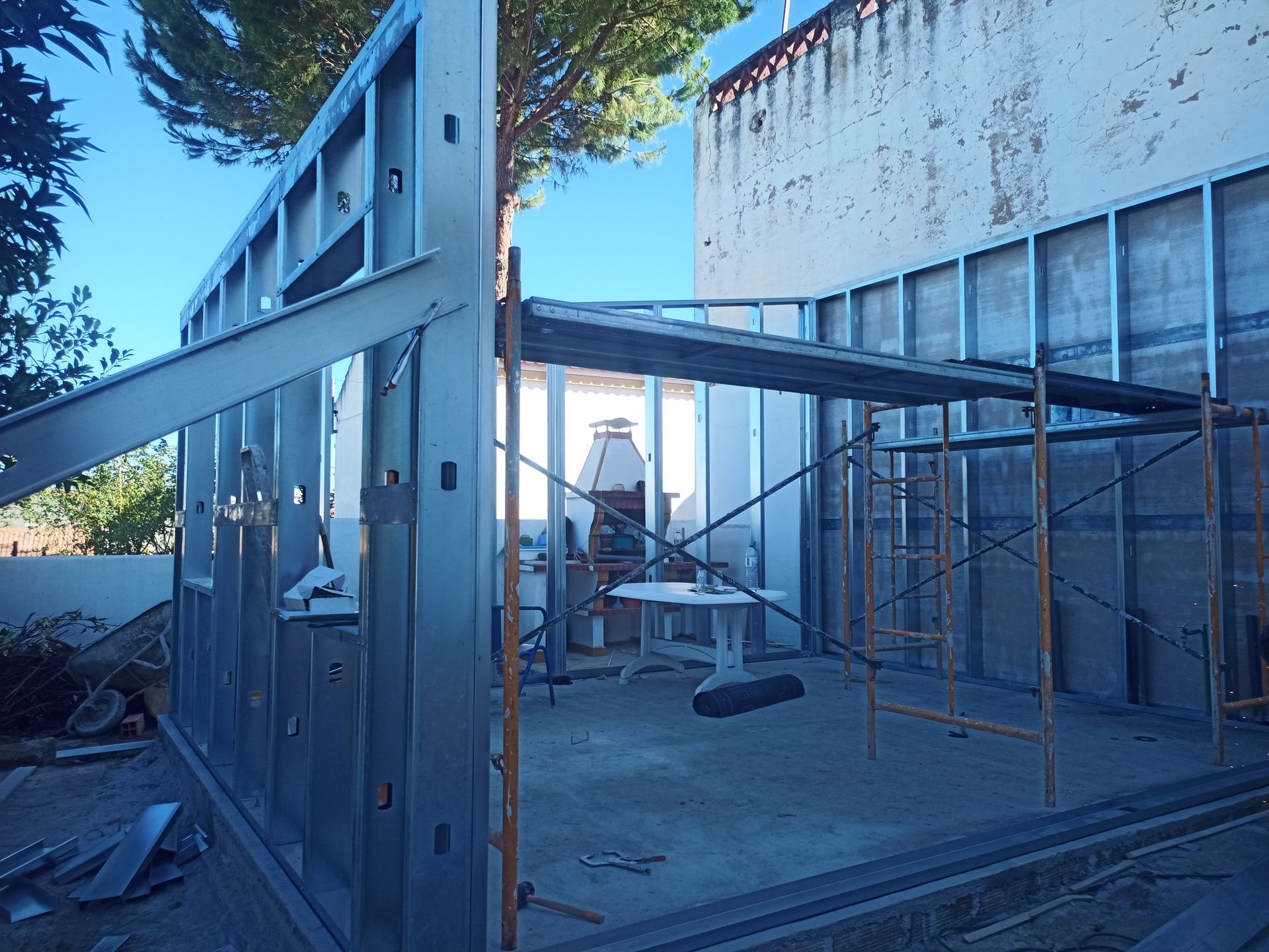 Estrutura metálica de um edifício em construção, andaimes, piso de concreto, contra uma parede branca.